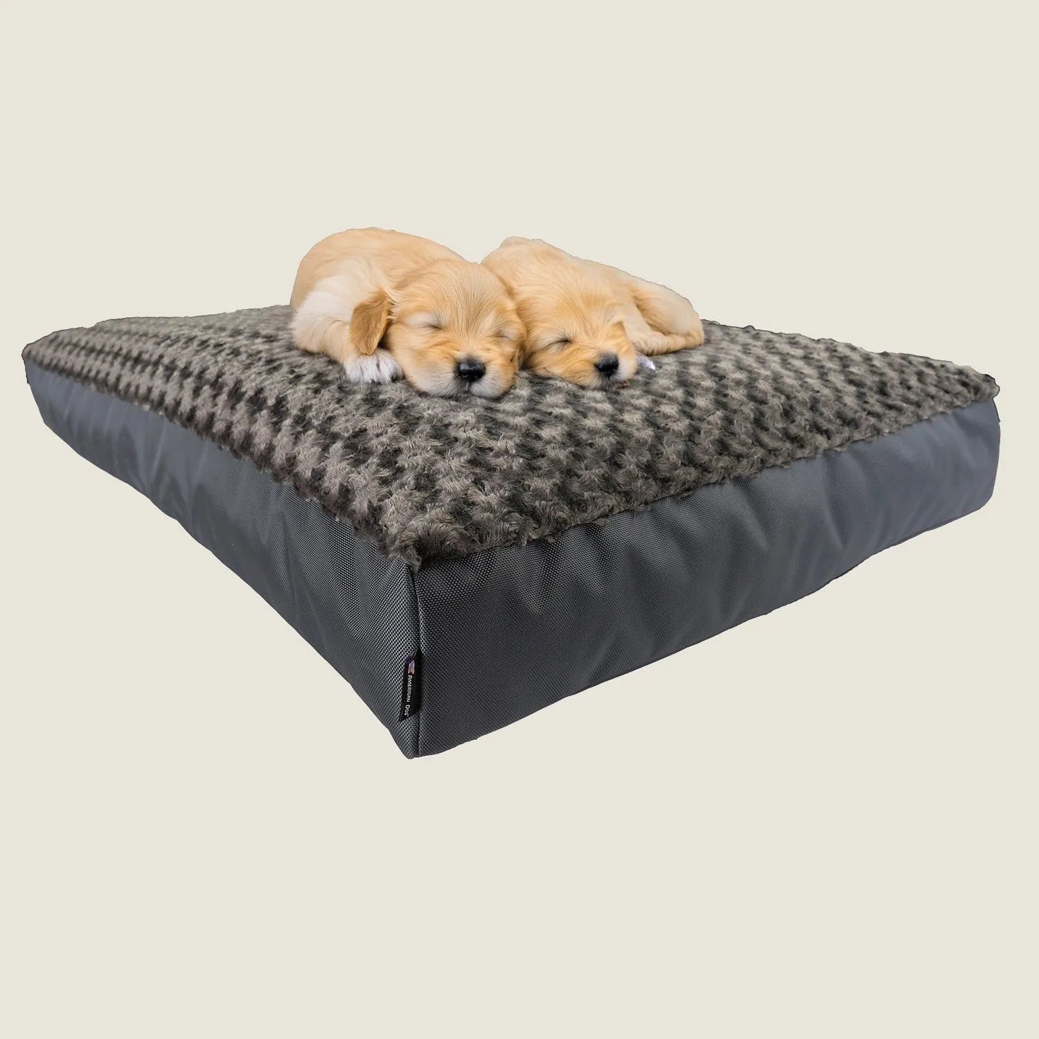 Two golden puppies sleeping on a plush, gray orthopedic dog bed with a soft, patterned top.
