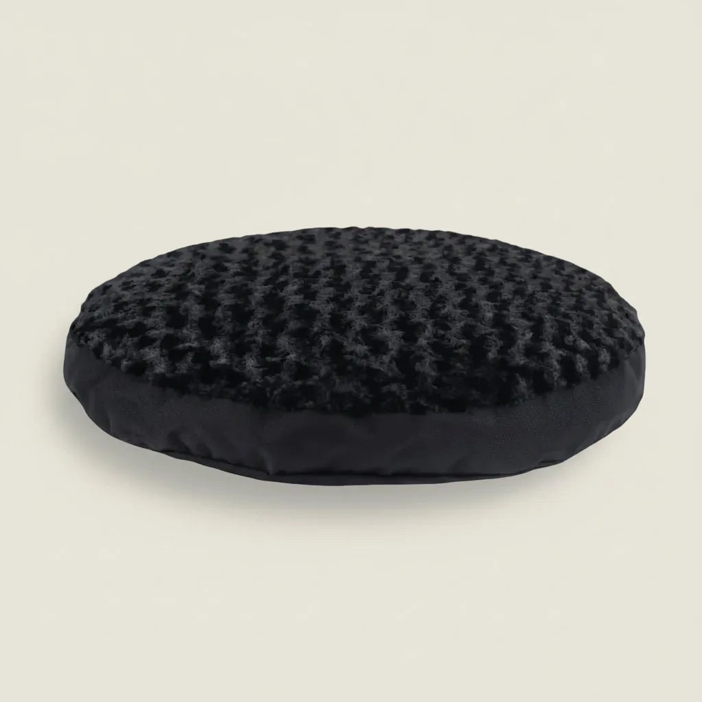 Round black dog bed with a soft raised fur texture and smooth nylon base, designed for comfort and support.
