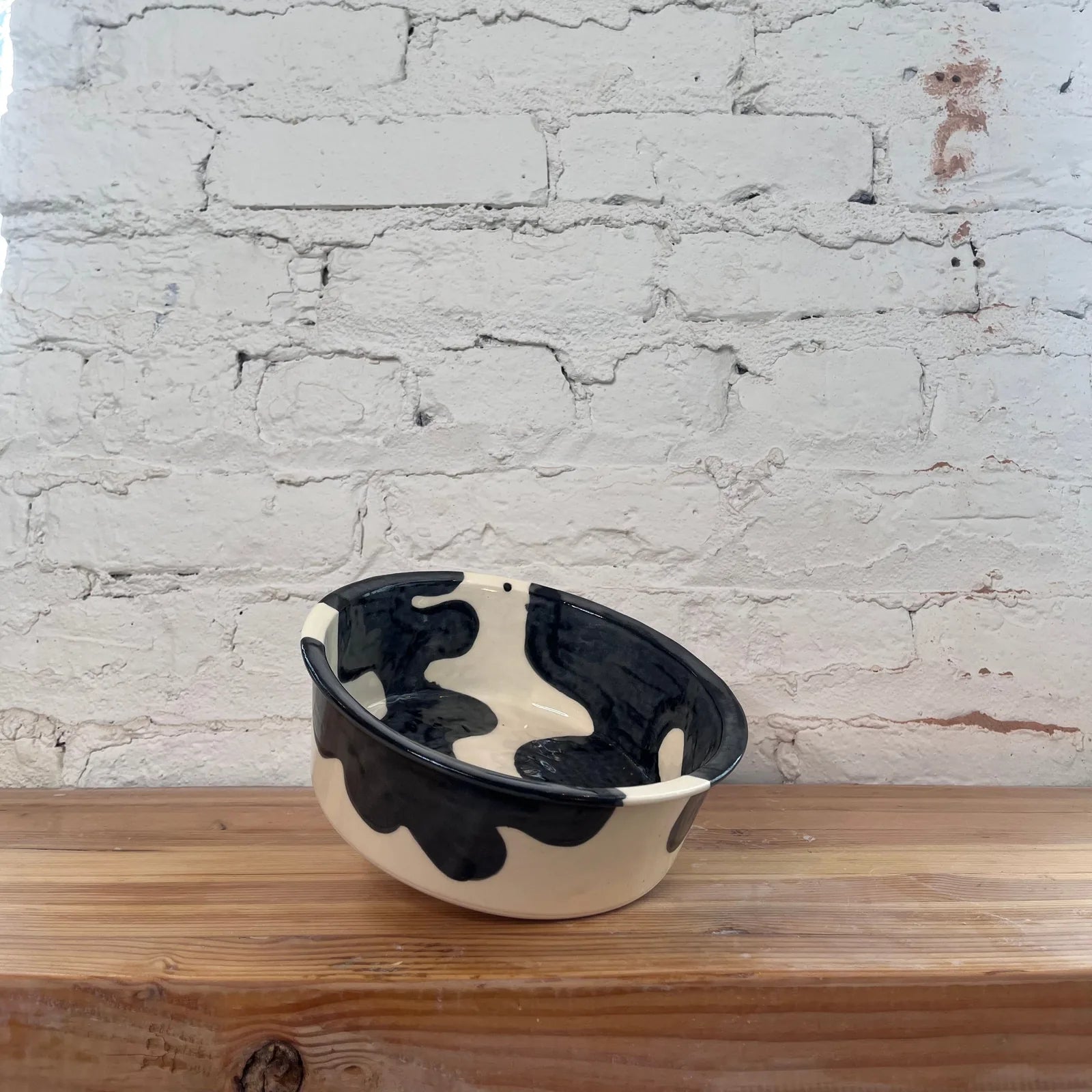 Handmade ceramic dog bowl with a unique black and cream cow print design, measuring 7.5 inches wide.