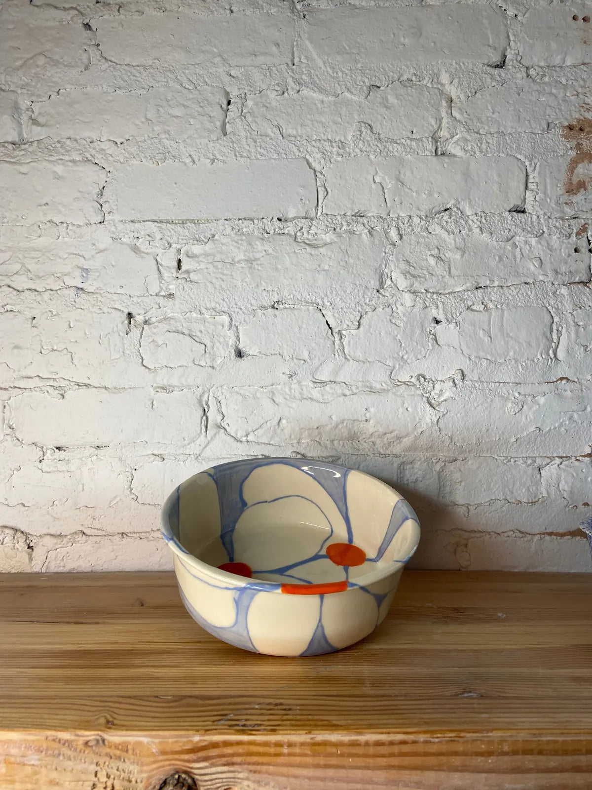Hand-painted ceramic dog bowl with a floral design in cream, blue, and orange, set on a wooden surface.