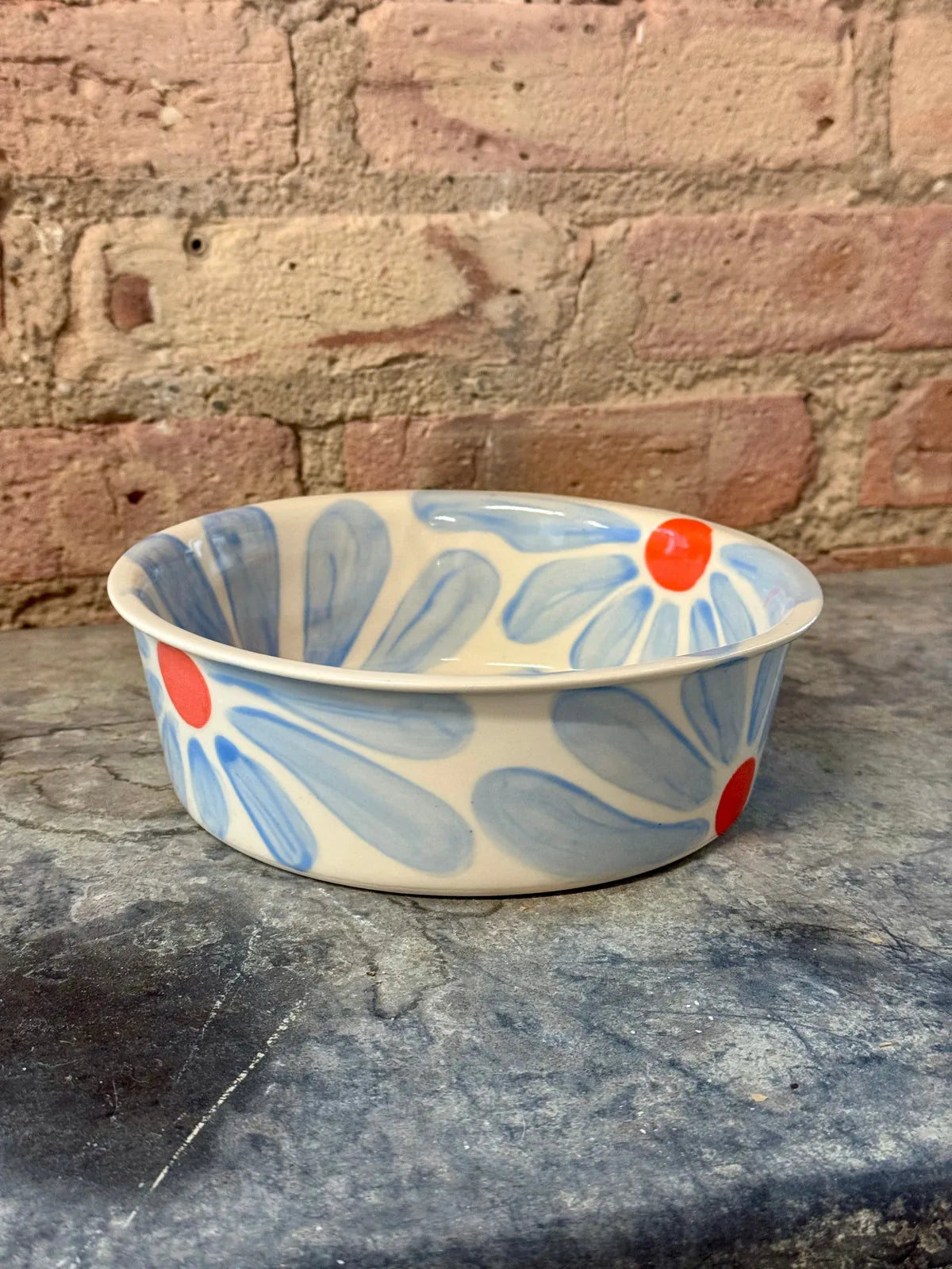 Hand-painted ceramic dog bowl features blue flower petals and a red center, adding charm to mealtime.