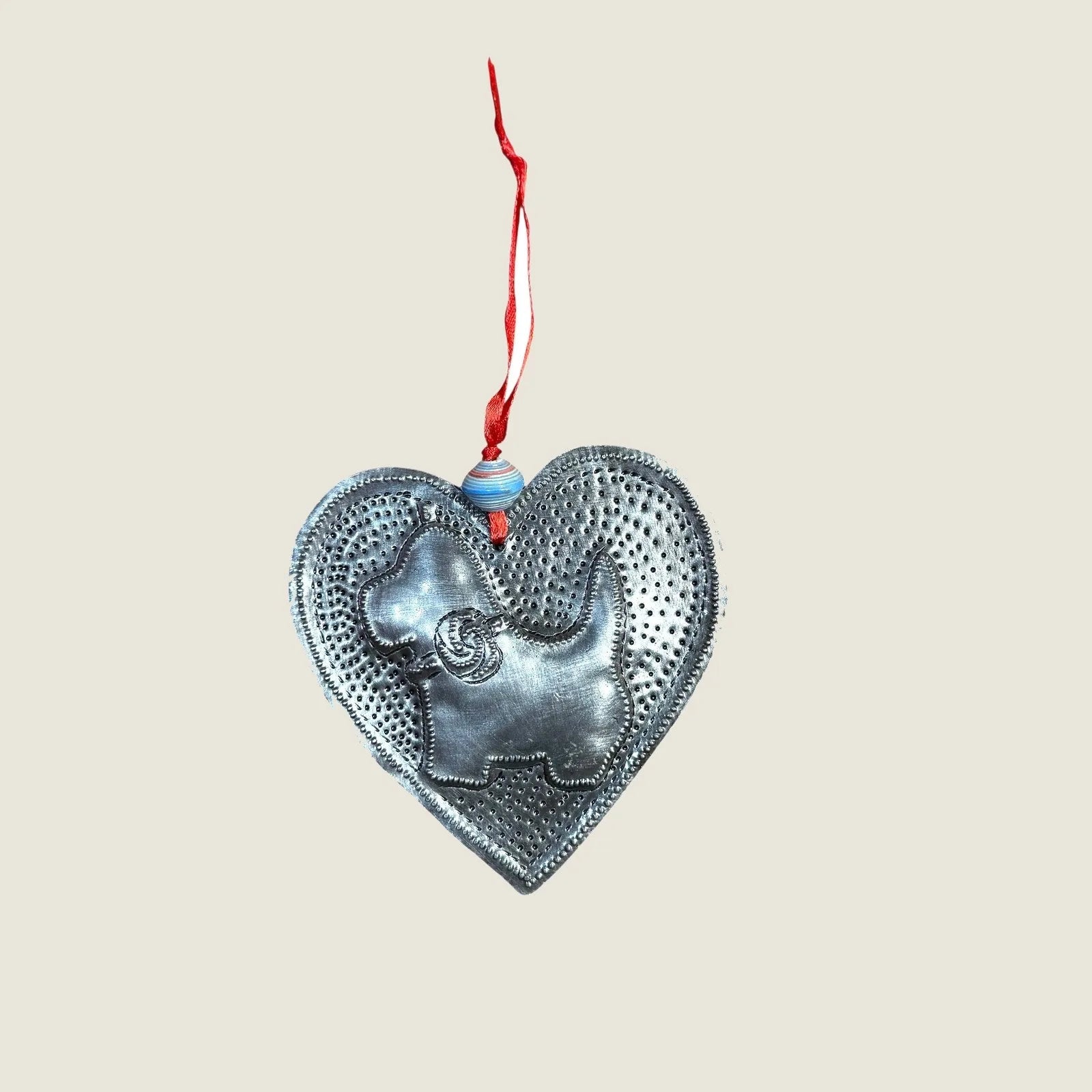 Handcrafted silver heart ornament featuring a dog silhouette, made from recycled steel with a red hanging ribbon.