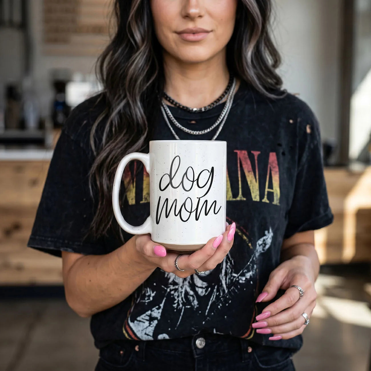 White 16oz ceramic mug with black "dog mom" graphic, held by a person in a vintage tee, showcasing a cozy moment.