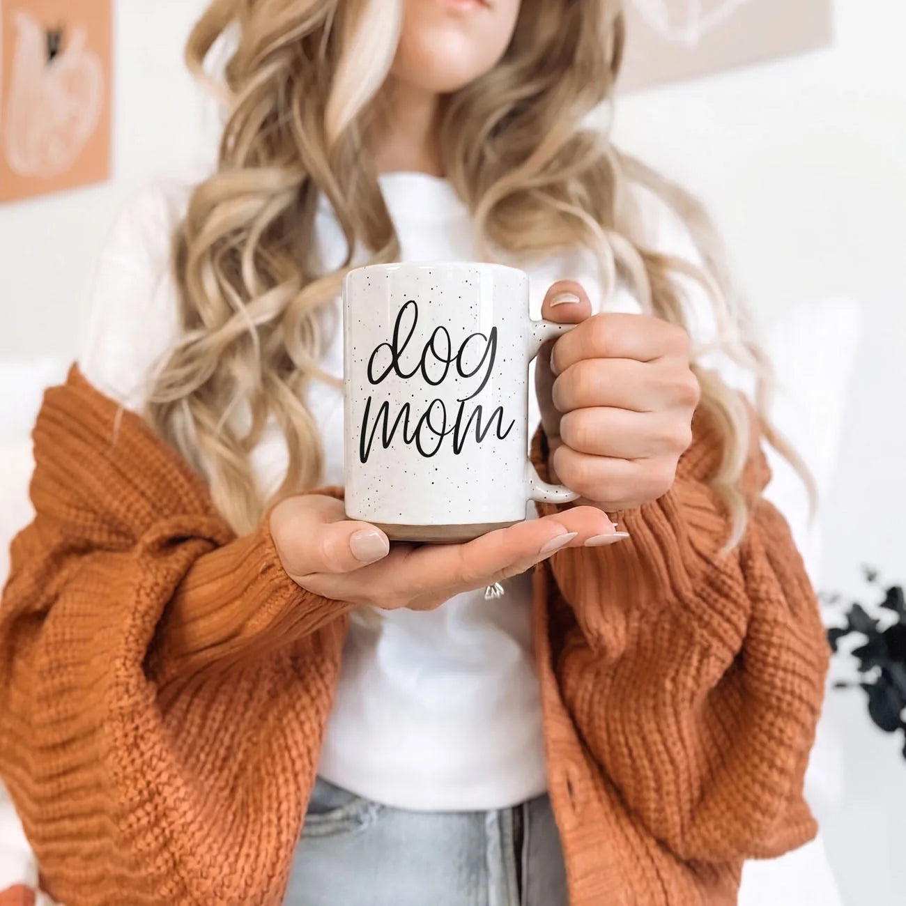 Ceramic 16oz mug with "dog mom" graphic, off-white with dark speckles, held by a woman in a cozy orange sweater.