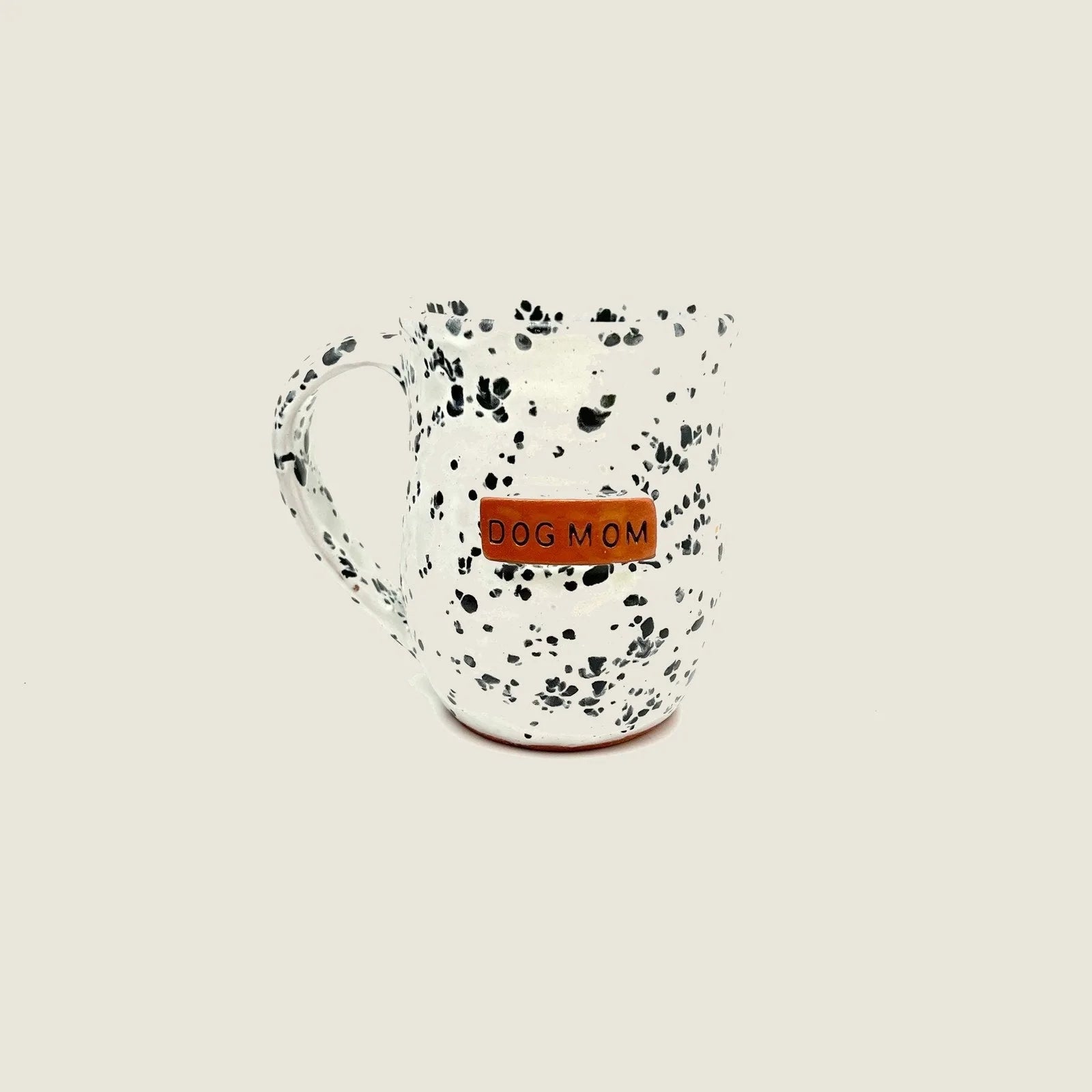 Handmade ceramic mug with black and white speckled design and a "DOG MOM" tag, crafted from Haitian clay.