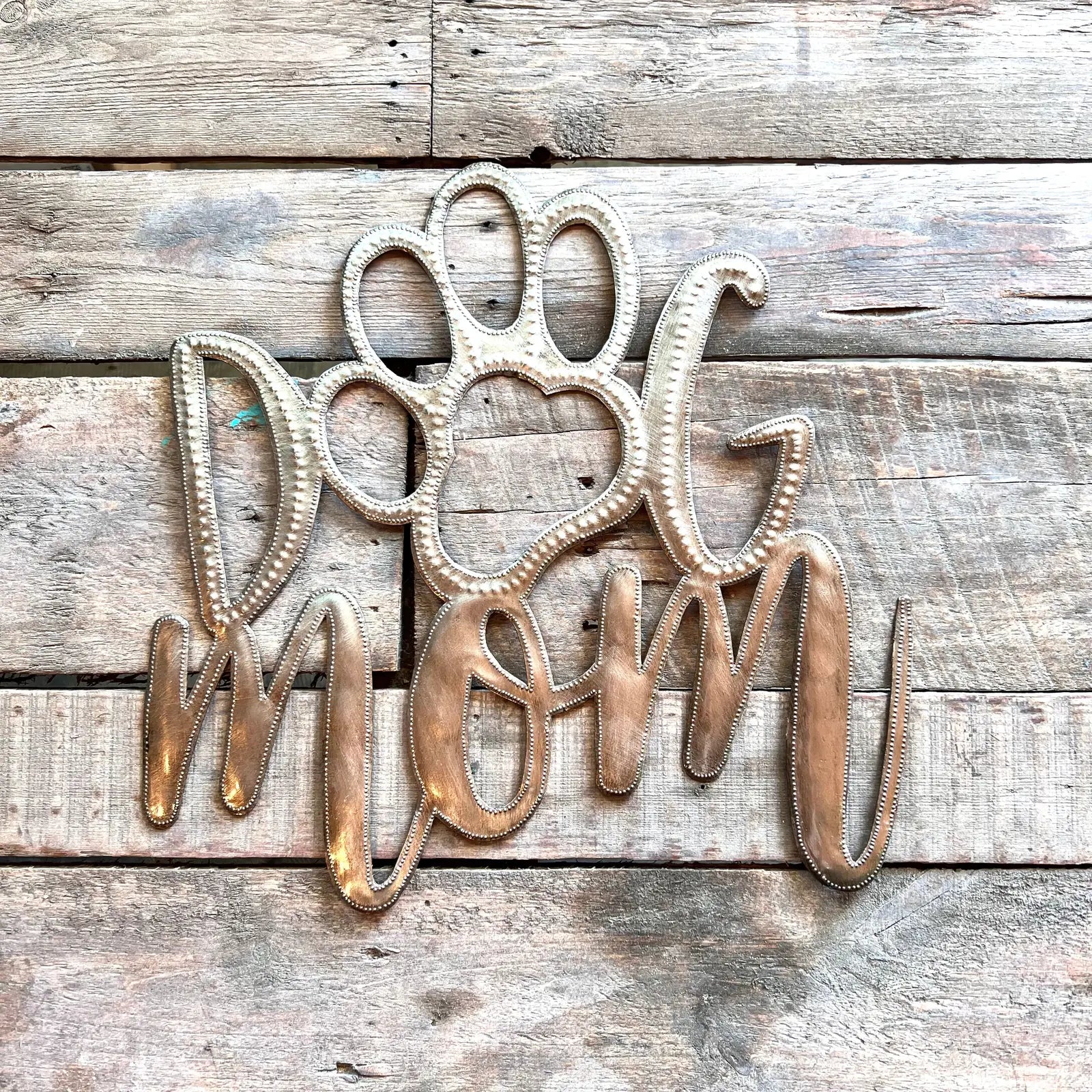 Handcrafted metal art reading "Dog Mom," featuring a paw print, made from recycled Haitian steel.