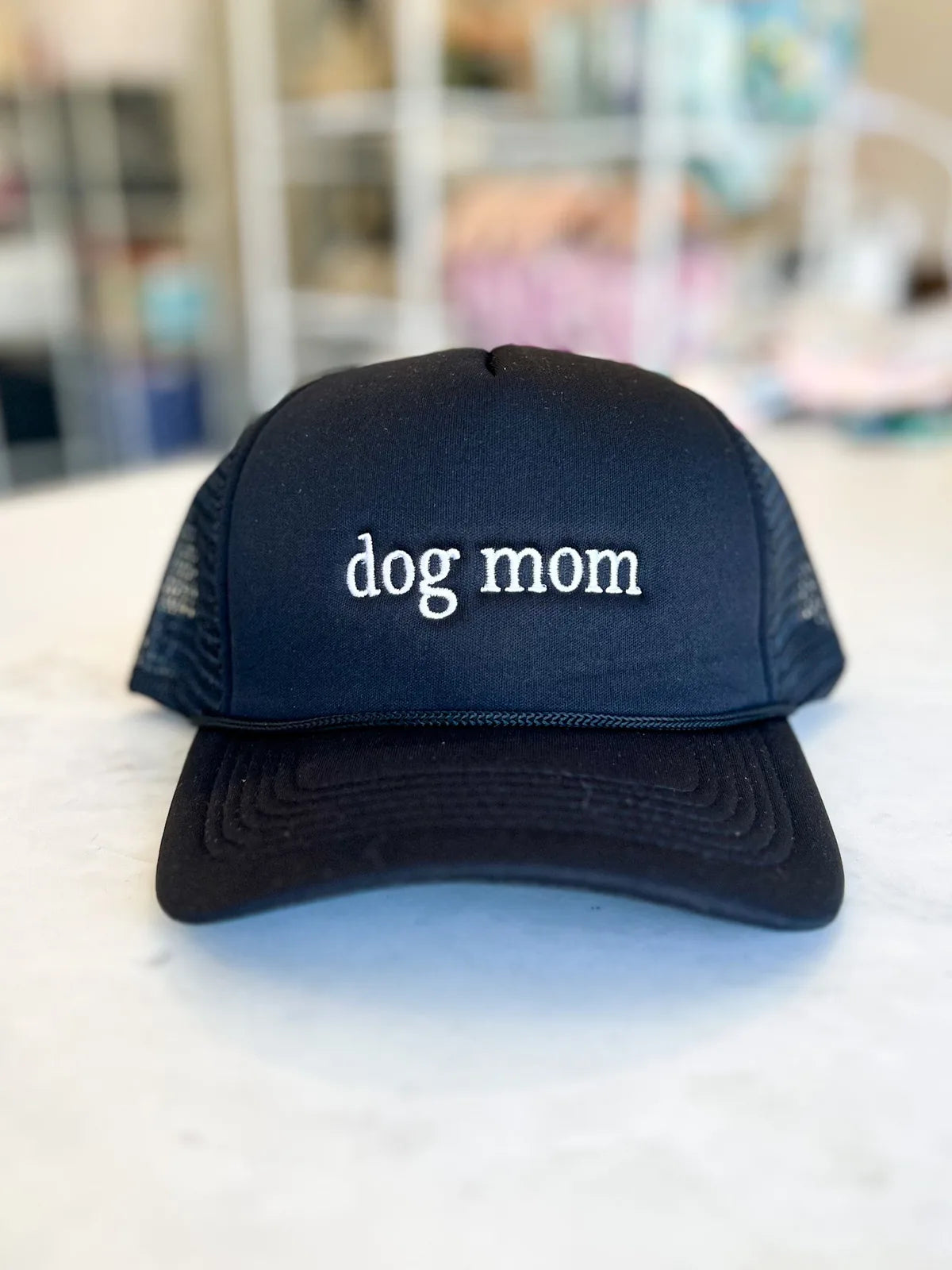 Black trucker hat with embroidered "dog mom" text, featuring a structured front and adjustable mesh back.