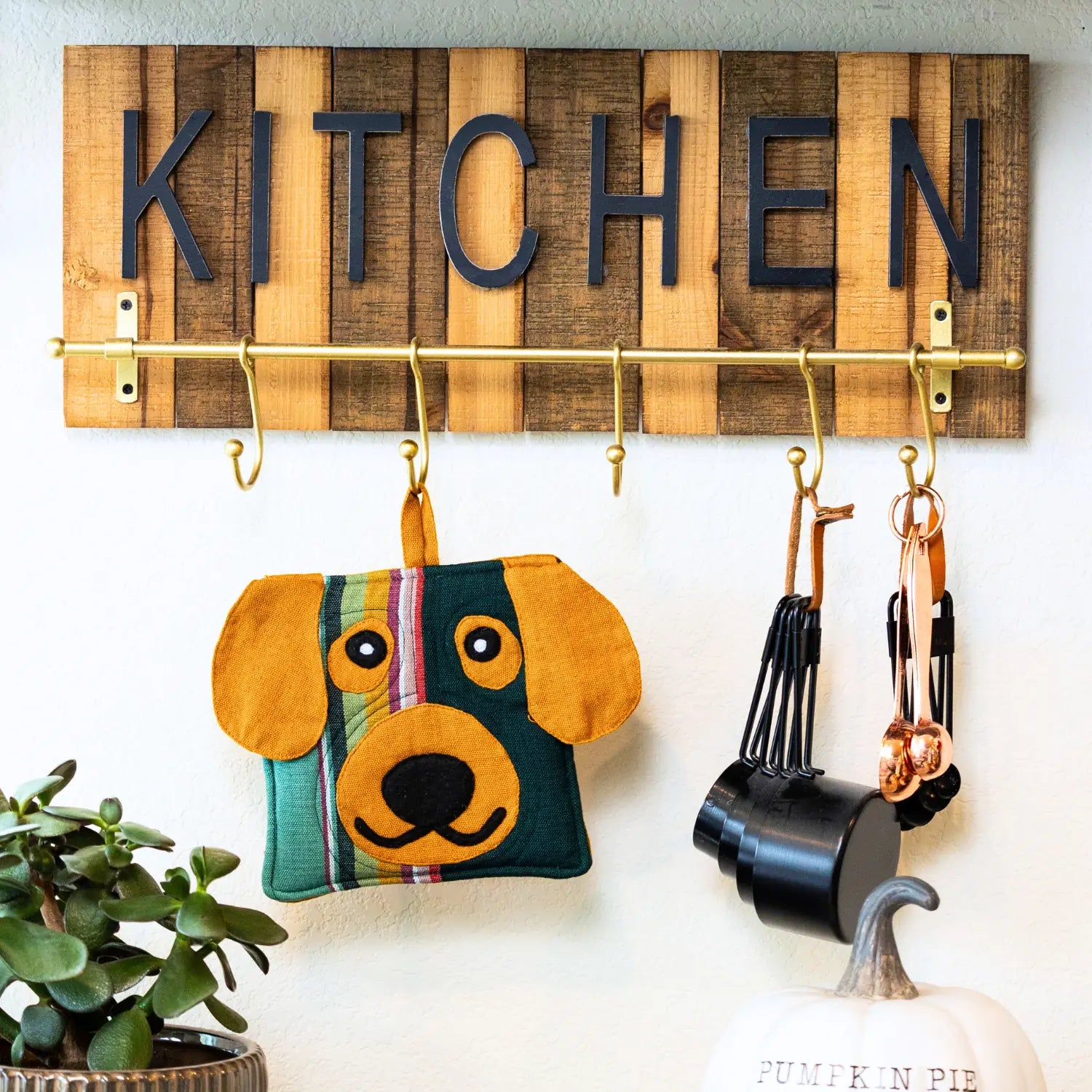 Handcrafted dog-shaped pot holder in bright colors, hanging from a kitchen rack with utensils and a succulent nearby.