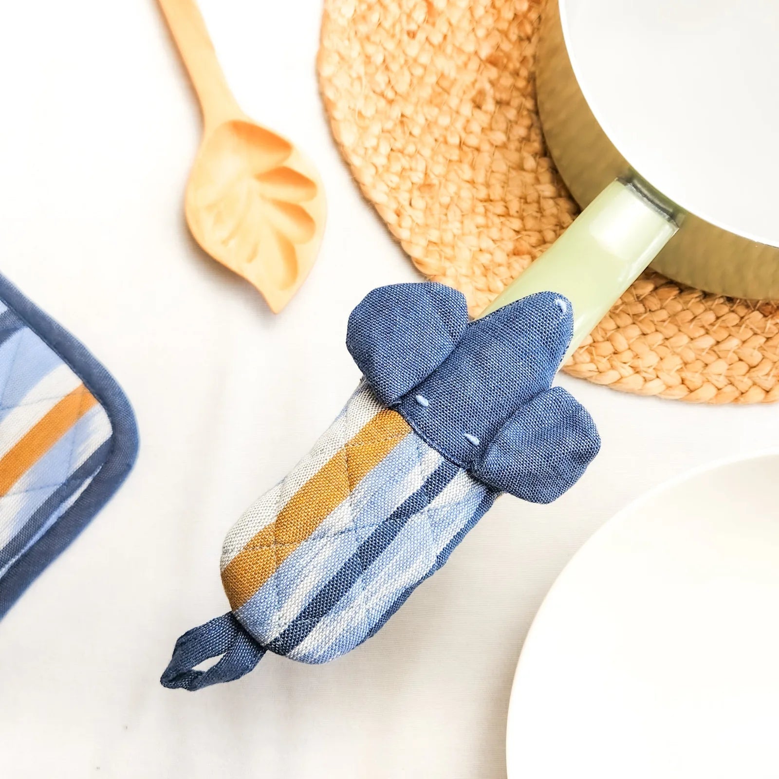 Dog-shaped skillet handle holder in blue cotton with stripes, resting on a pot handle for heat protection.