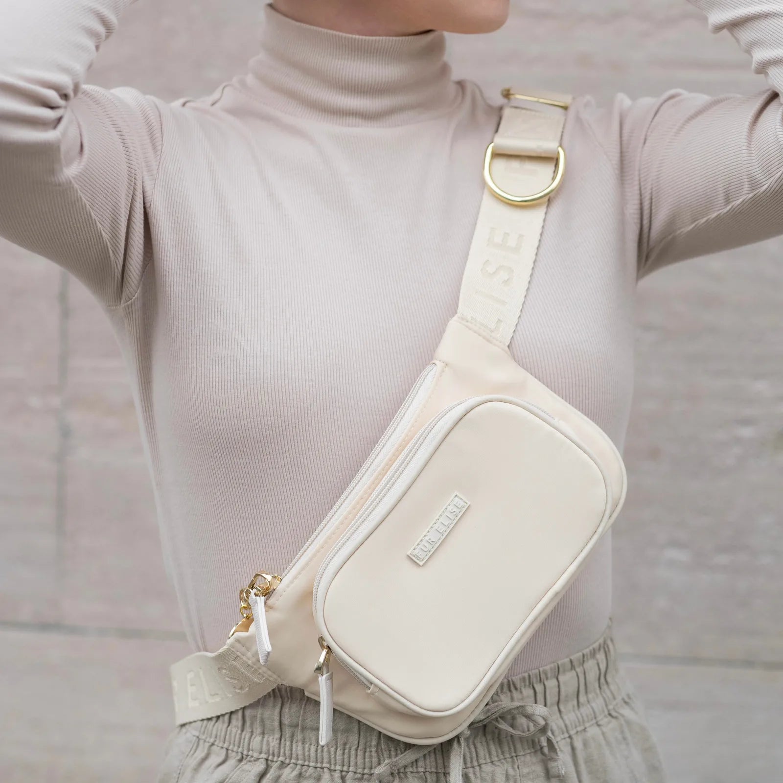 Lightweight beige Elise Galleria dog walking bag worn as a belt bag, featuring gold hardware and multiple zippered pockets.