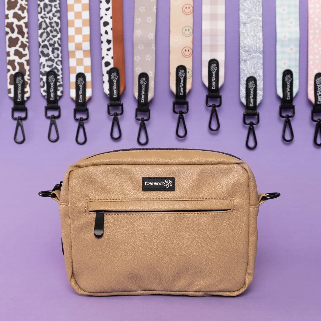 Faux leather nude dog owner essentials bag with a zipper pocket, showcased against colorful patterned straps on a purple b...