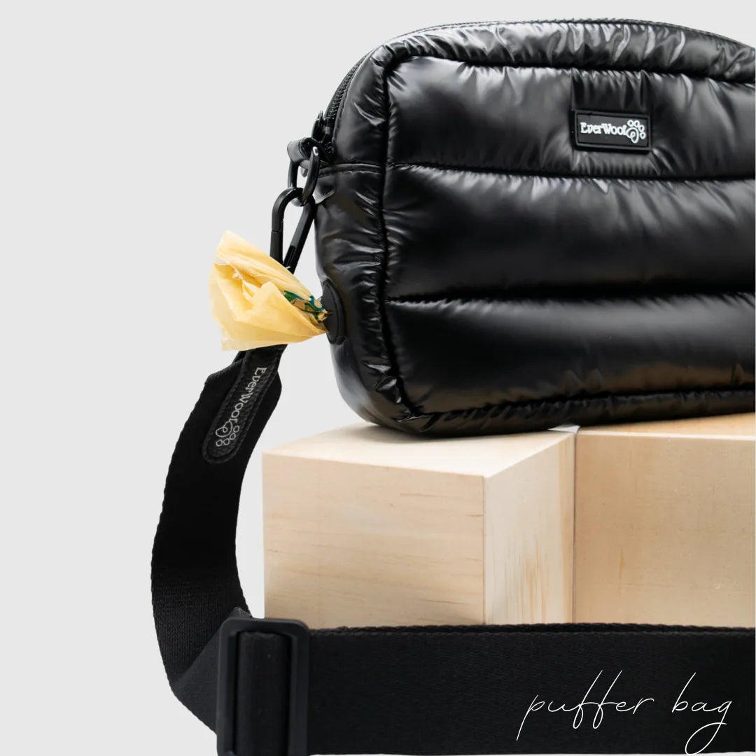 Black puffer bag with a yellow poop bag dispenser, resting on wooden blocks, showcasing its stylish and functional design.