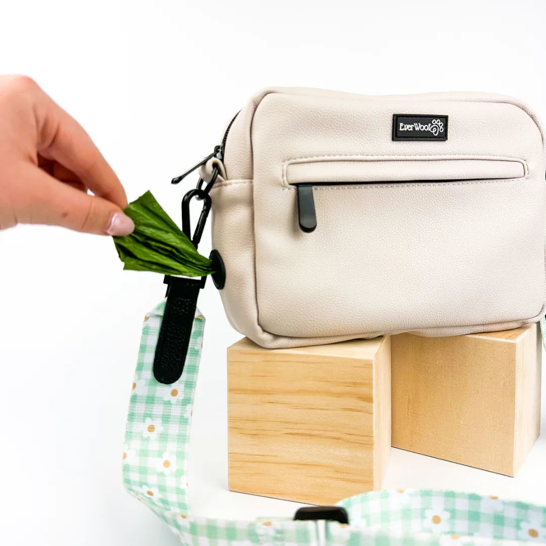 Light beige faux leather dog owner essentials bag with green plaid strap, displaying a poop bag dispenser.