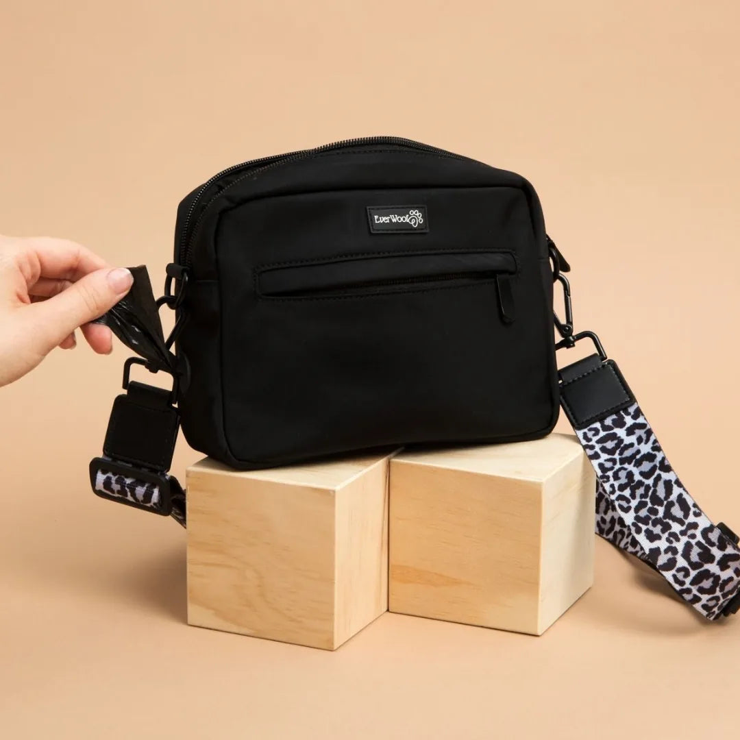 Black EverWoof Doggy Owner Essentials Bag with leopard-print strap, resting on wooden blocks.