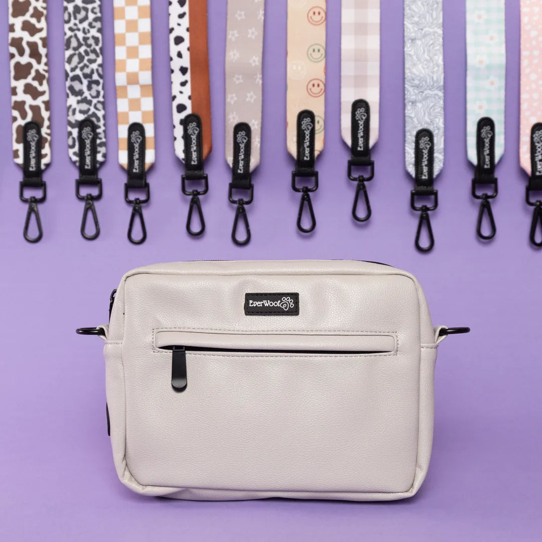 Light grey faux leather dog owner essentials bag with zipper pockets, displayed against a purple background.