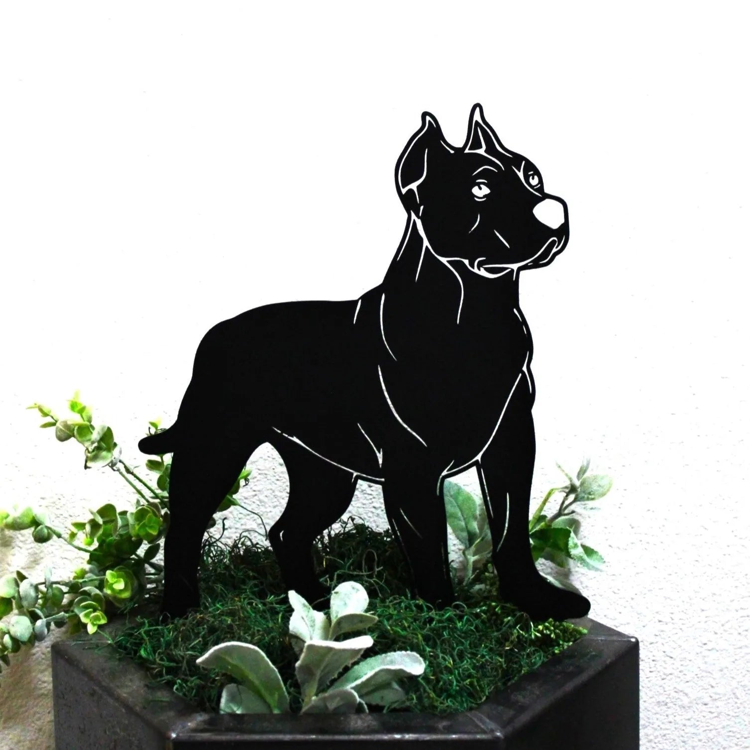Dogo Argentino metal silhouette in matte black, standing among green foliage in a decorative pot.