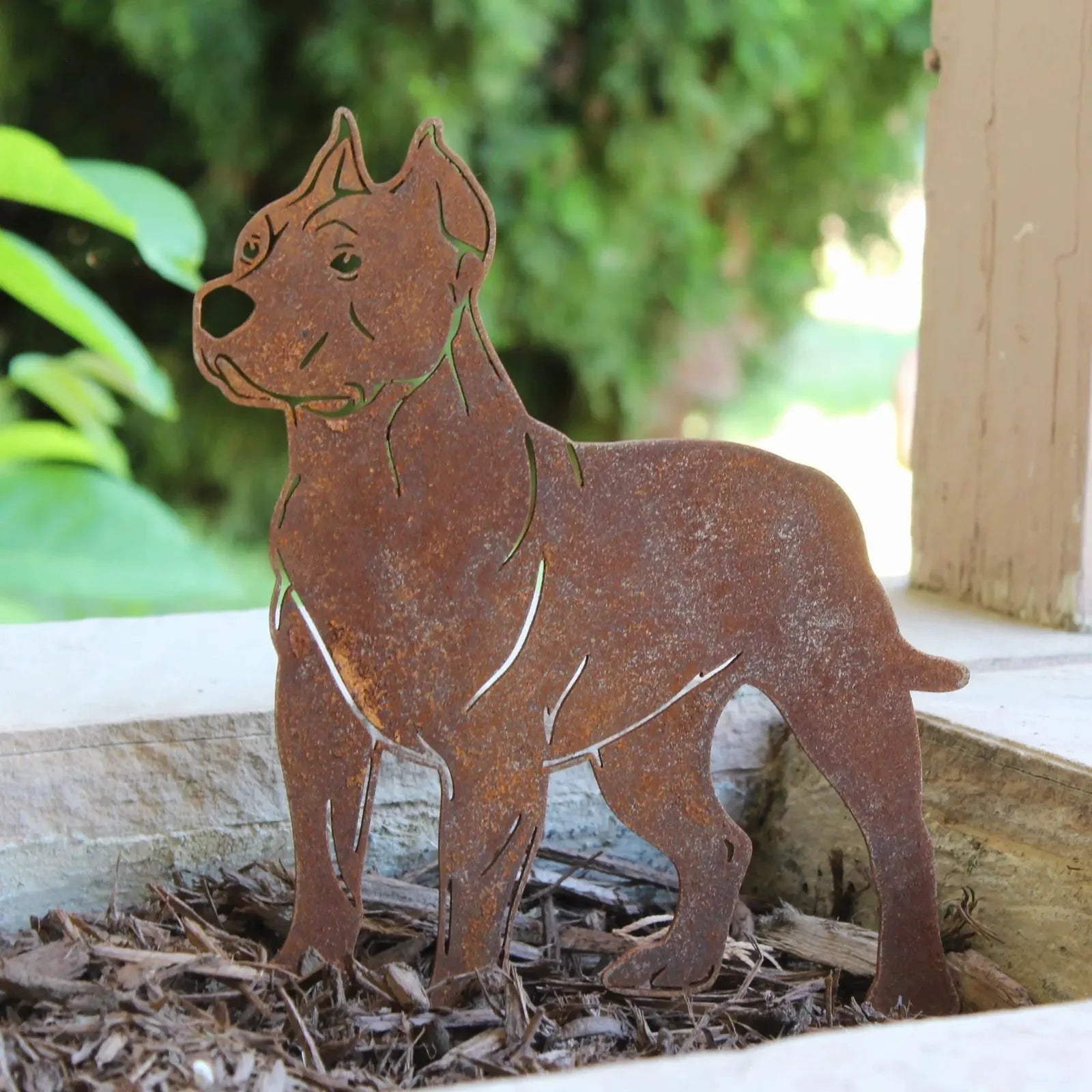 Rust-colored Dogo Argentino metal silhouette standing on mulch, featuring cut-out details and a sturdy design.