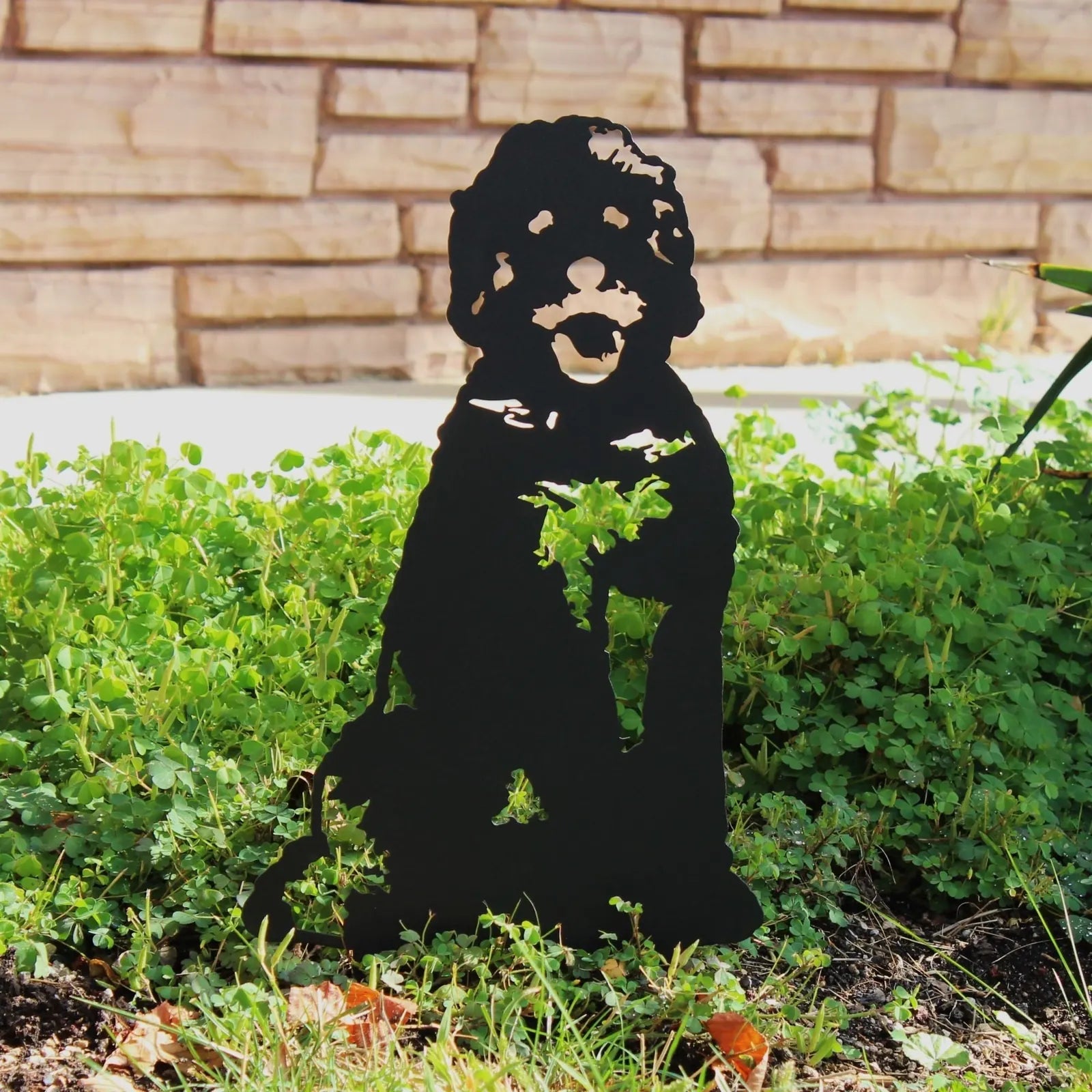 Black metal dog silhouette art standing among green foliage, ideal for outdoor decor.