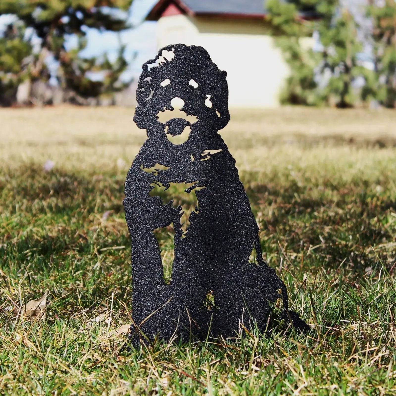 Black metal silhouette of a seated Doodle dog on grassy outdoor terrain, showcasing intricate cutouts.
