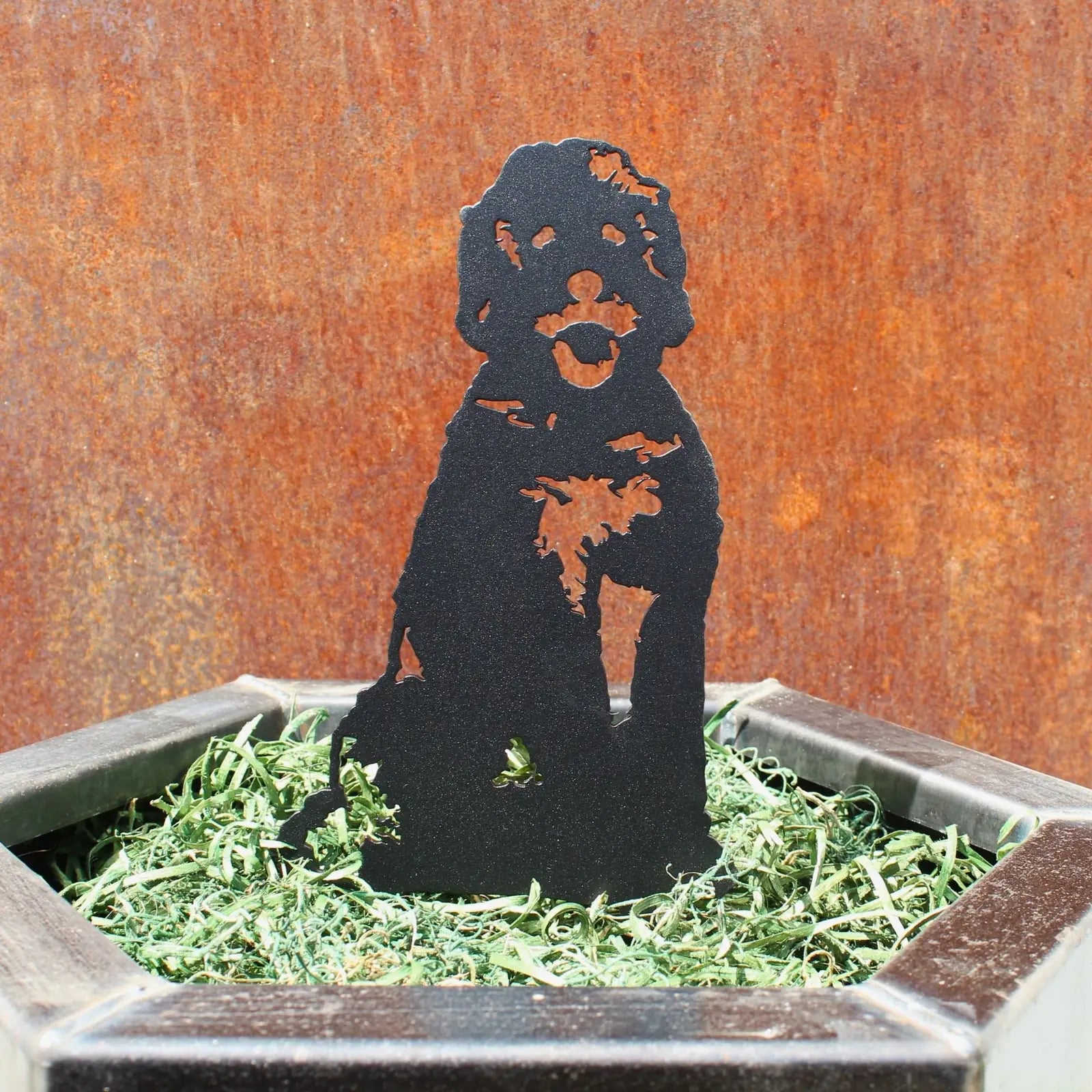 Black metal Doodle dog silhouette art sitting in green decorative moss within a hexagonal pot.