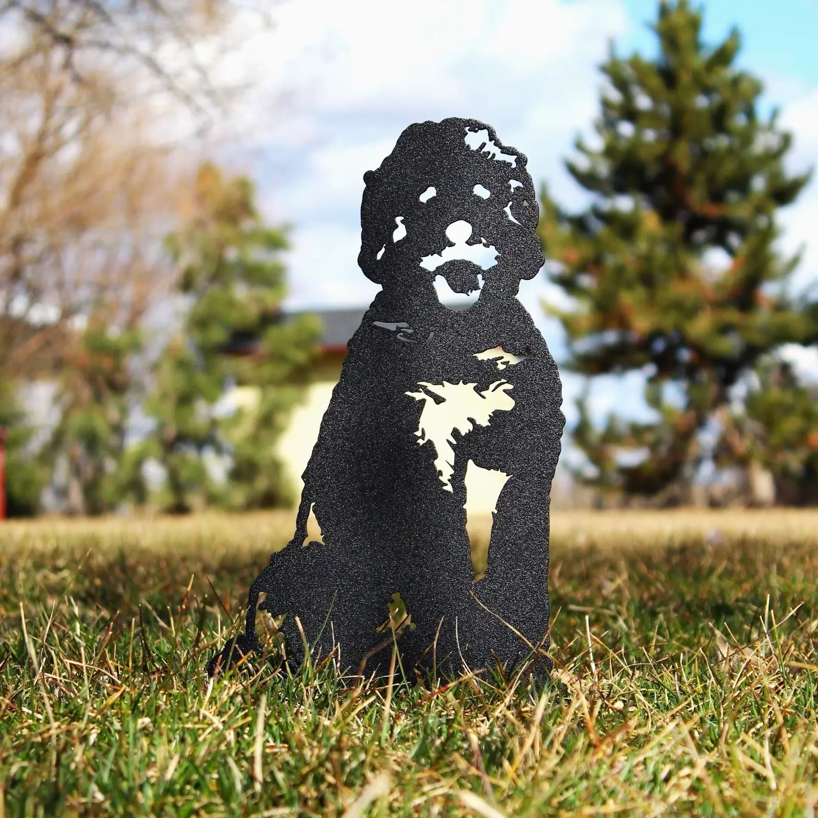 Black metal silhouette of a Doodle dog sitting in a grassy outdoor space, showcasing detailed craftsmanship.