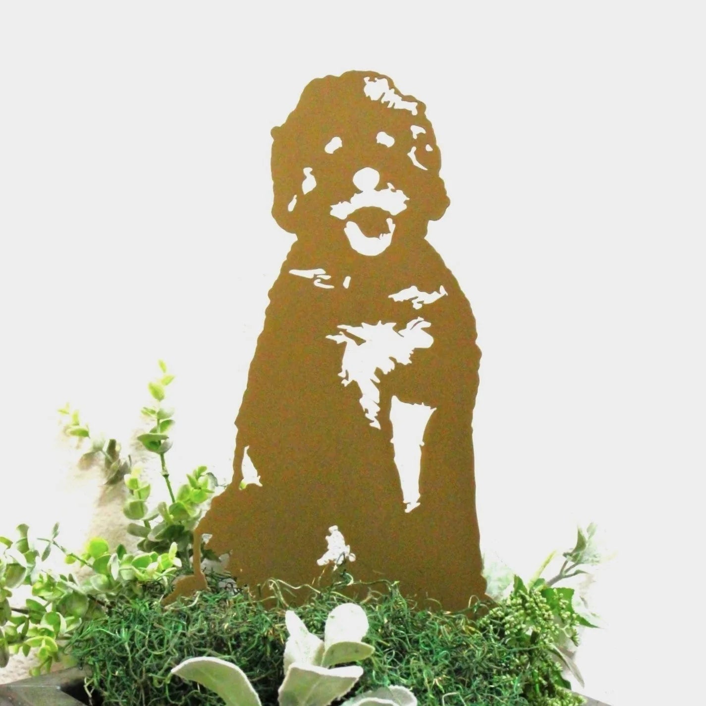 Doodle metal silhouette in Corten steel, depicting a dog sitting among green foliage, ideal for outdoor decor.