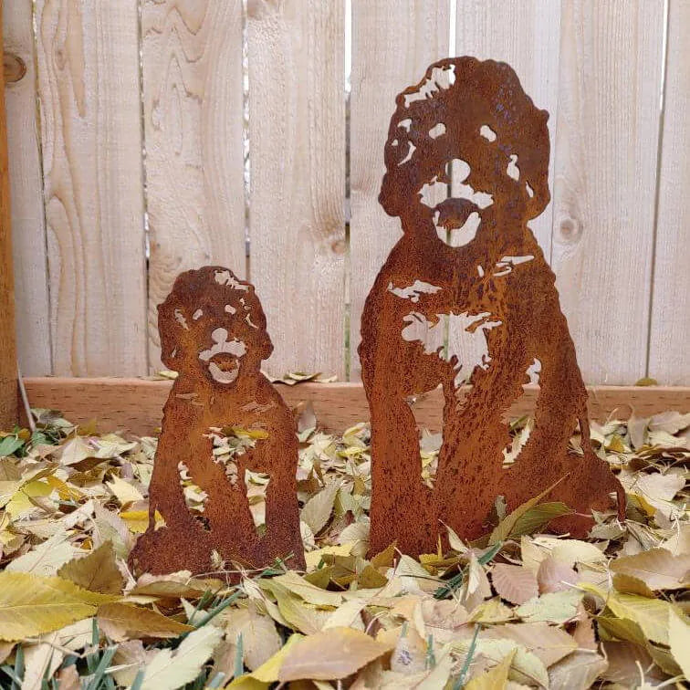 Rust-colored metal dog silhouettes, depicting a seated puppy and adult dog, surrounded by yellow autumn leaves.