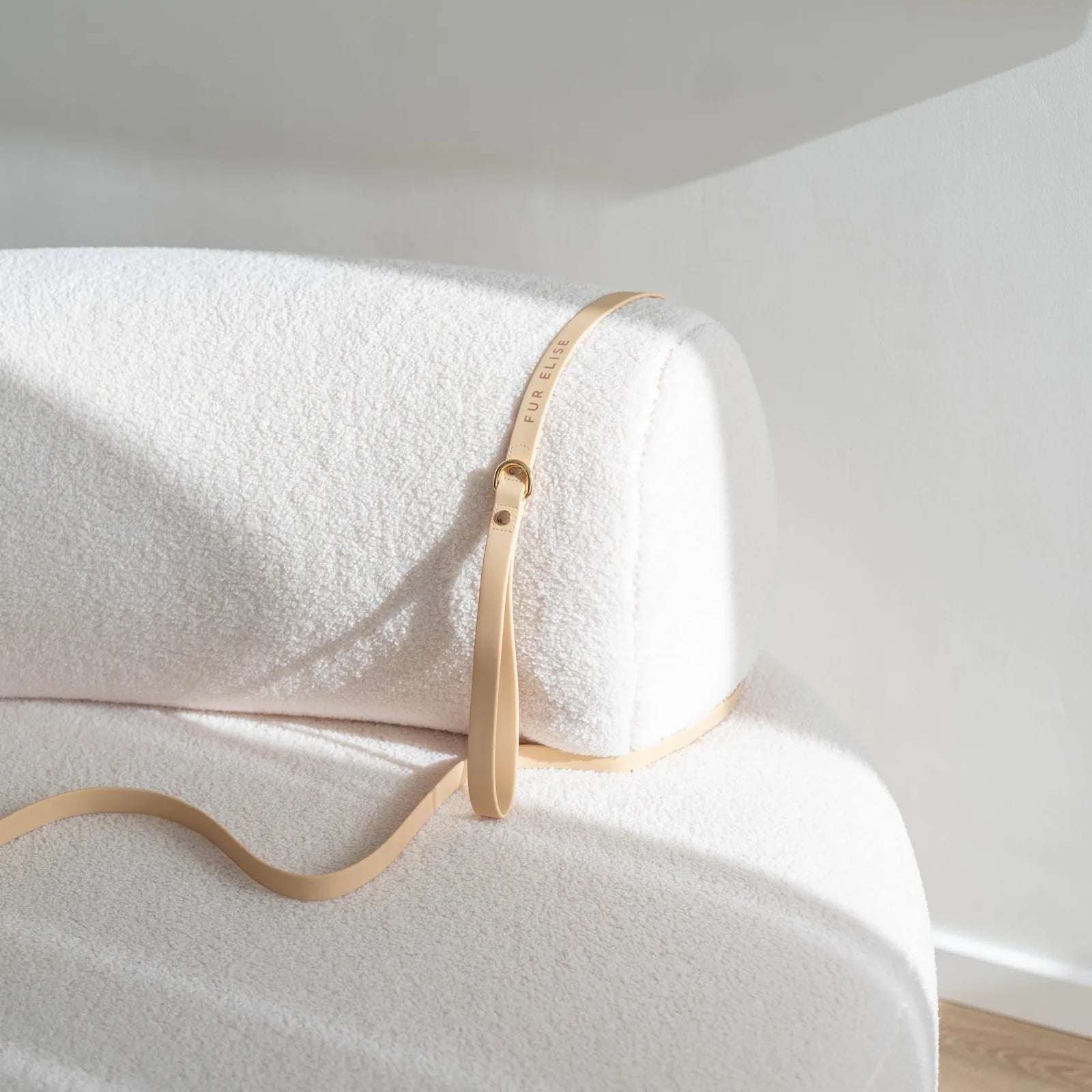 Elise leash in sand resting on a soft, light-colored fabric surface, showcasing its sleek design and gold hardware.
