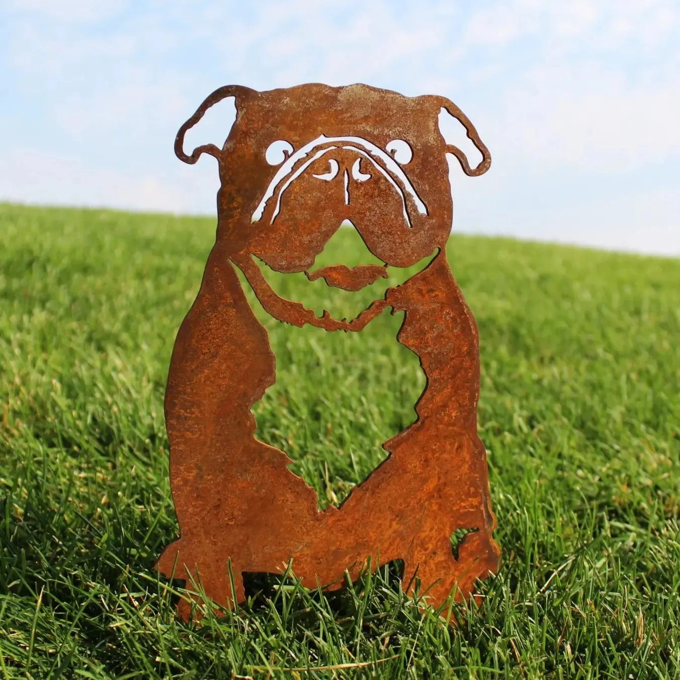 Rusty Corten steel silhouette of an English Bulldog standing in green grass, showcasing detailed facial features.