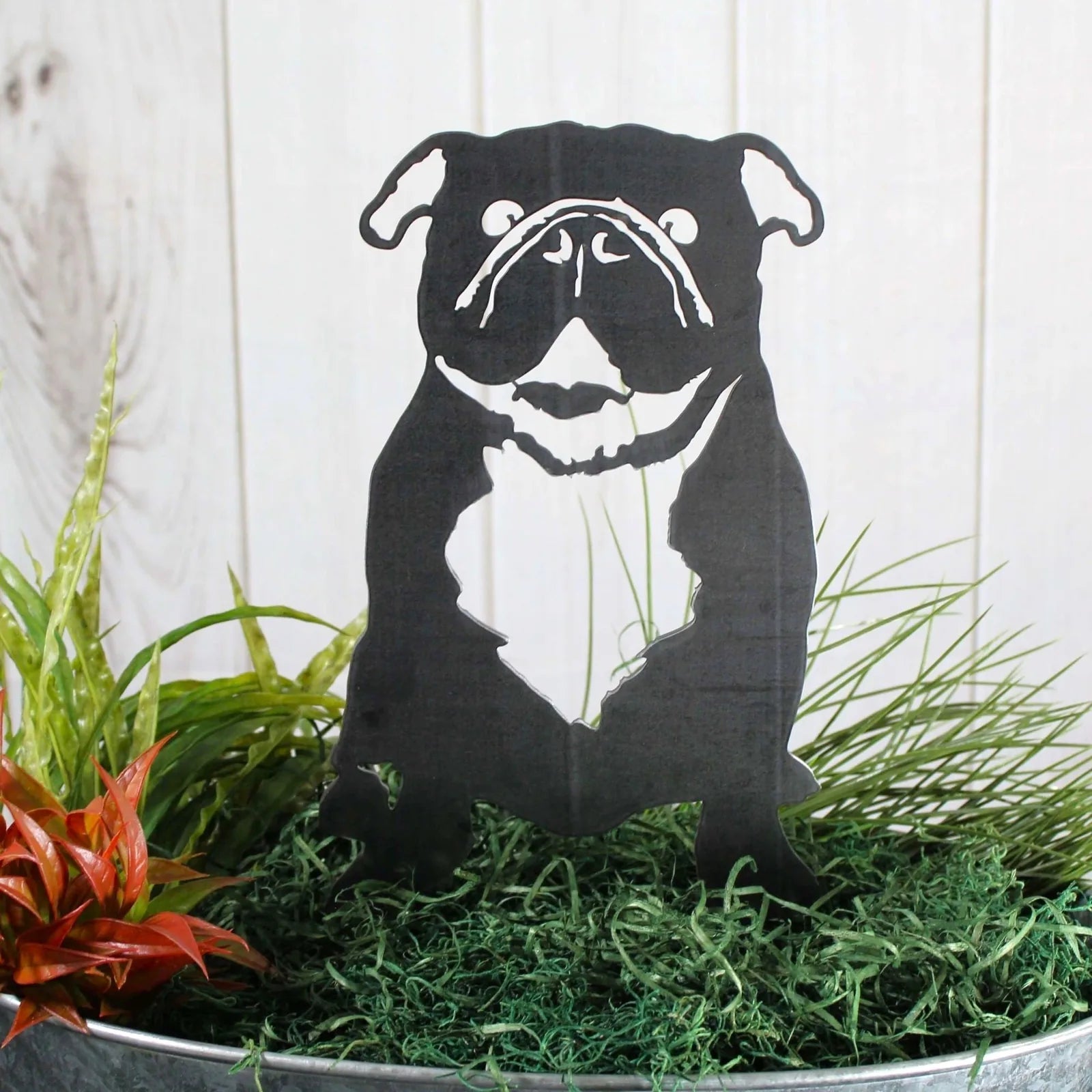 Black metal silhouette of an English Bulldog, displayed in greenery, perfect for outdoor dog decor.