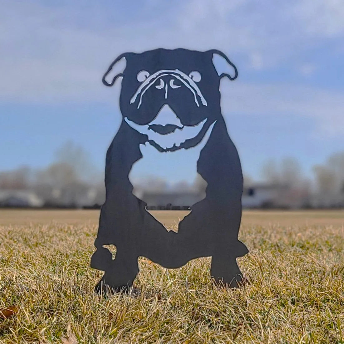 Black metal silhouette of an English Bulldog stands on grass, showcasing its distinct facial features and stout body.