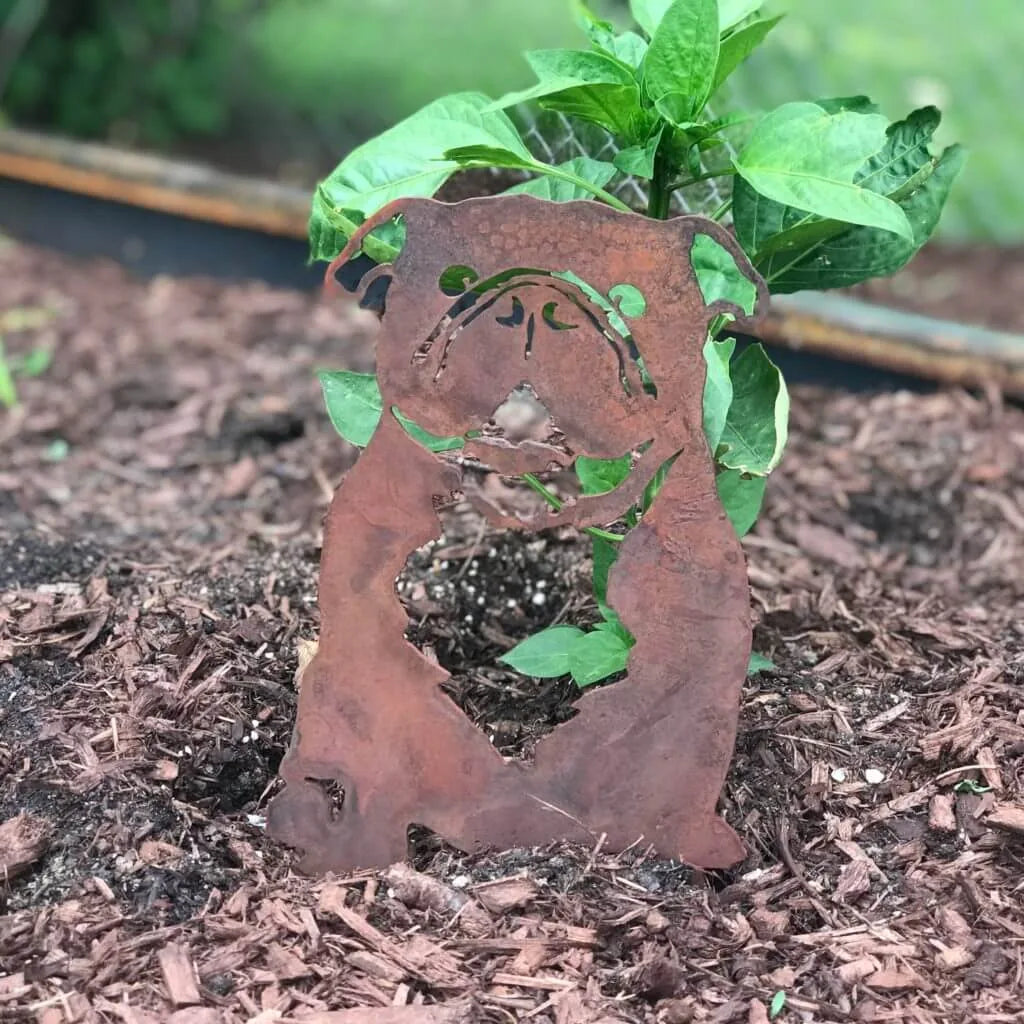 Rusty metal silhouette of an English Bulldog, nestled in garden mulch, surrounded by green leaves.