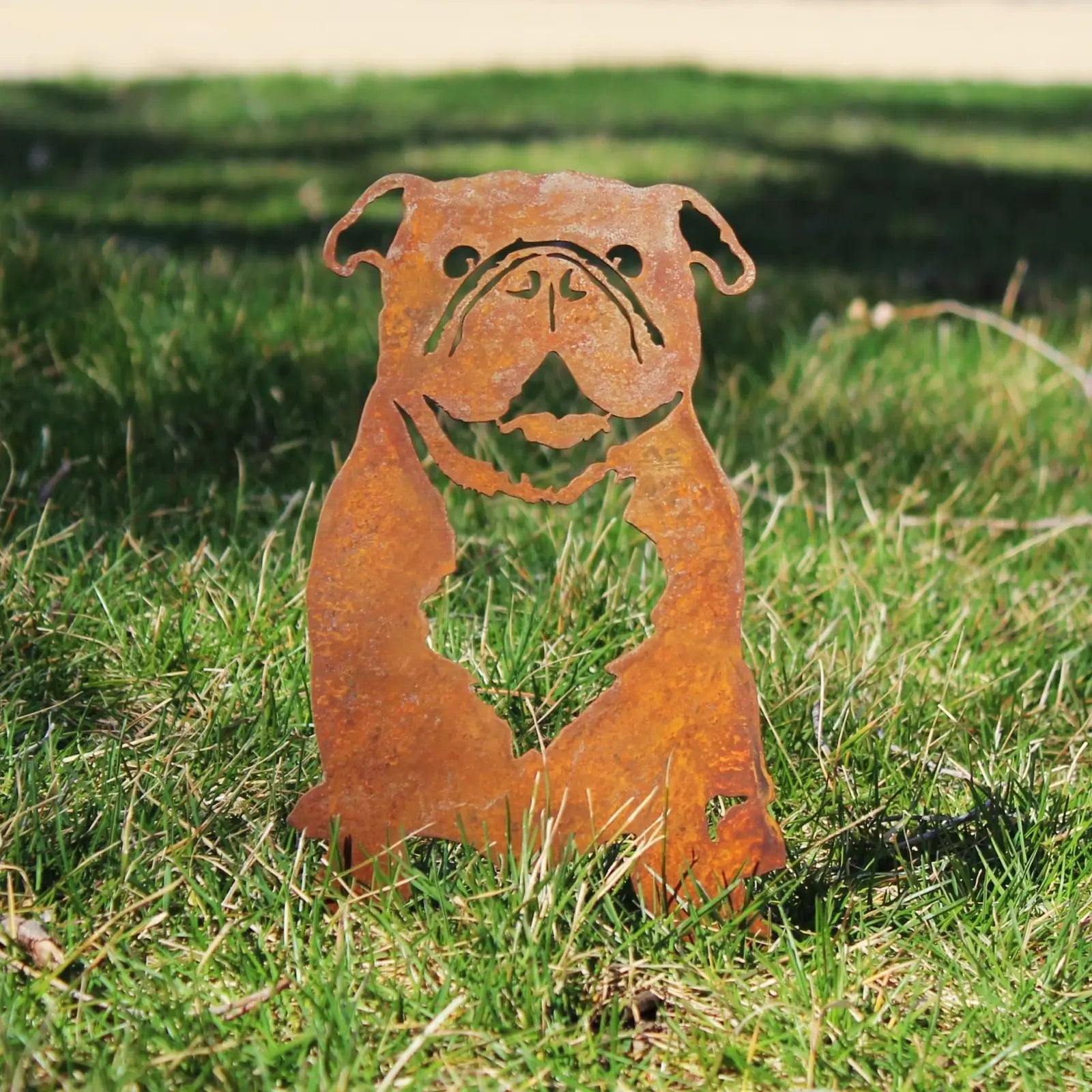 Rusty metal silhouette of an English Bulldog, showcasing intricate details, set against green grass background.