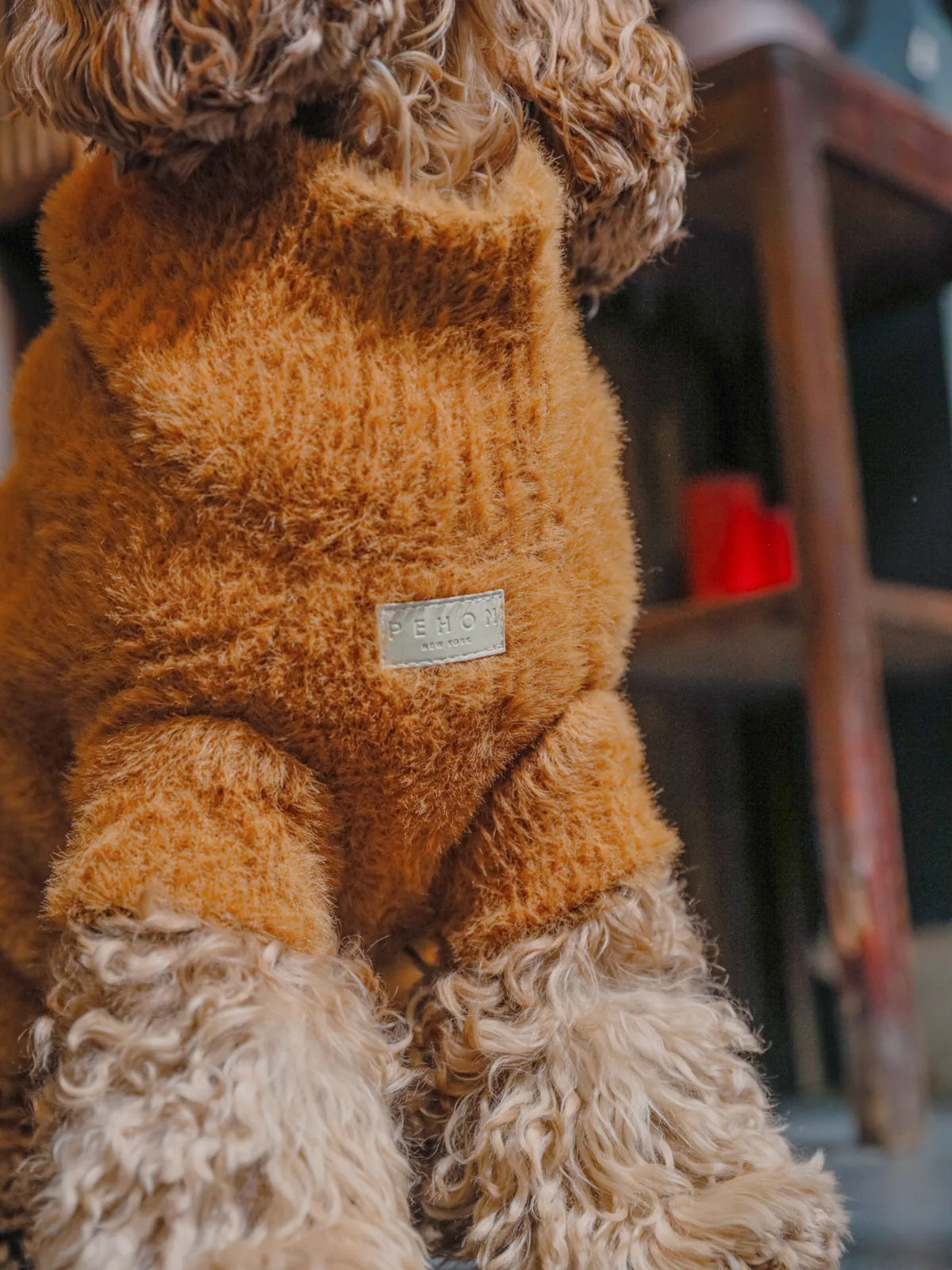 Cozy orange dog sweater with fuzzy texture, featuring a logo tag, designed for warmth and comfort.