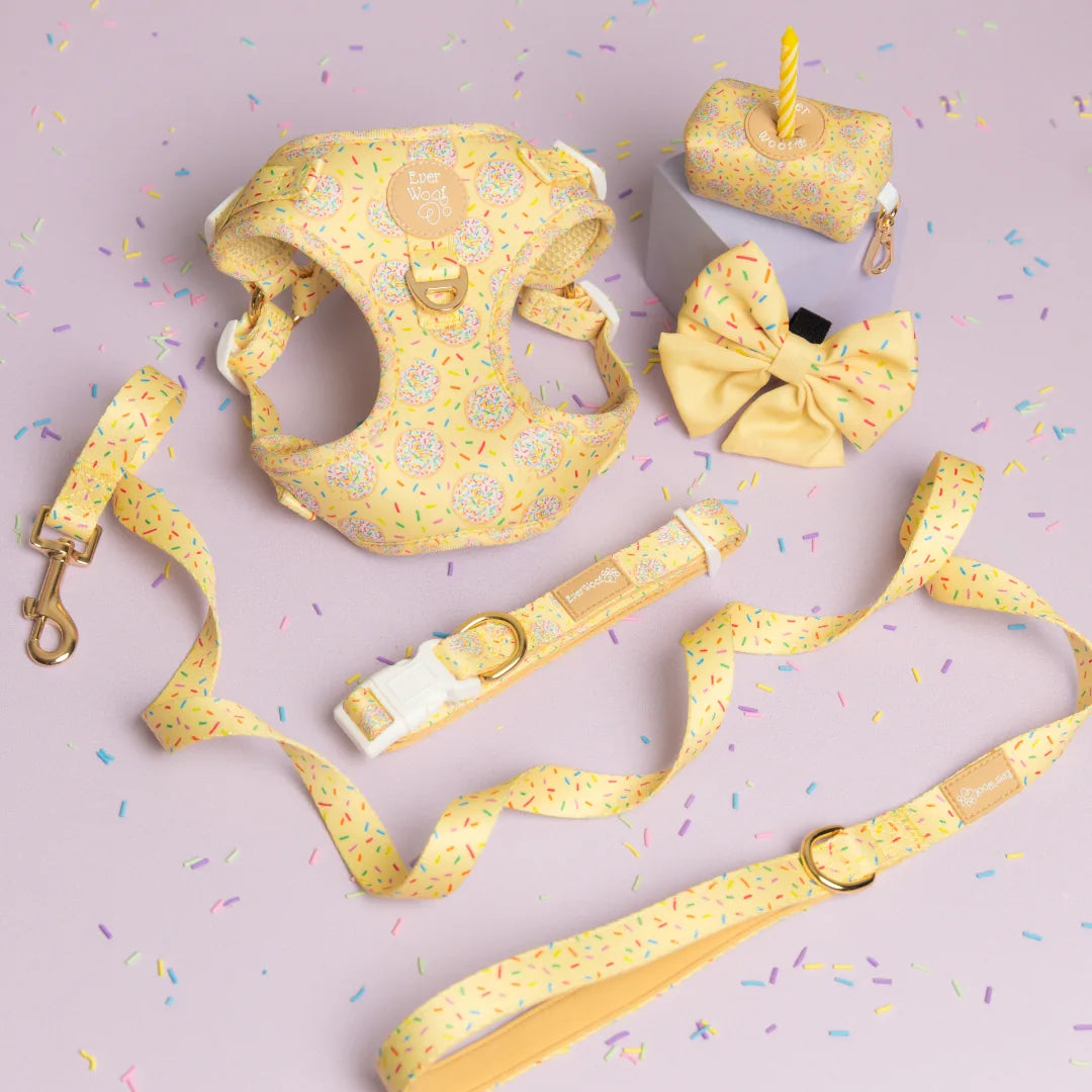 Yellow step-in dog harness with a playful cookie print, paired with matching leash and bow, set on a pastel background.