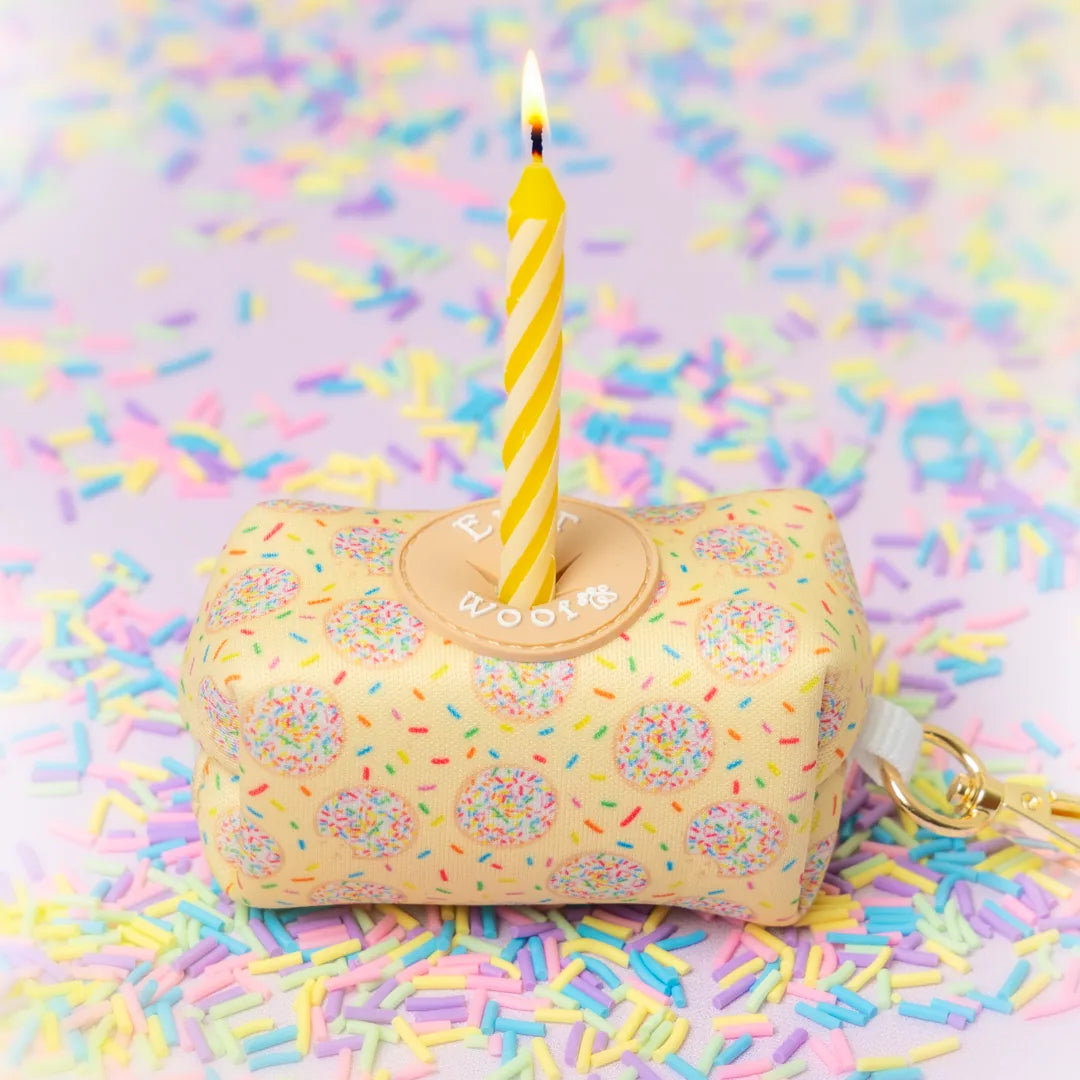 Neon yellow waste bag holder decorated with colorful sprinkles, topped with a yellow birthday candle, on a pastel pink bac...