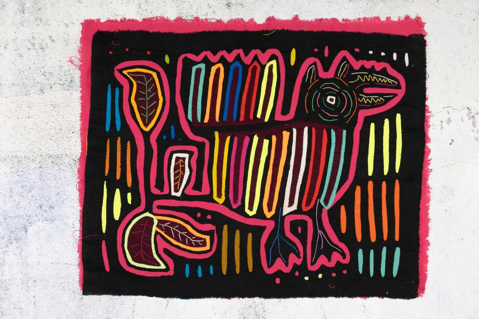 Colorful hand-stitched Mola featuring a dog design surrounded by vibrant geometric patterns on a black background.
