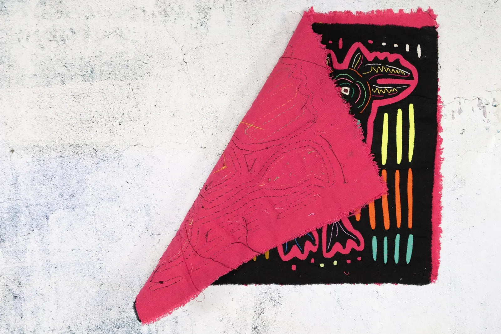 Colorful hand-stitched Mola textile featuring vibrant geometric patterns and a pink fringed edge on a black background.
