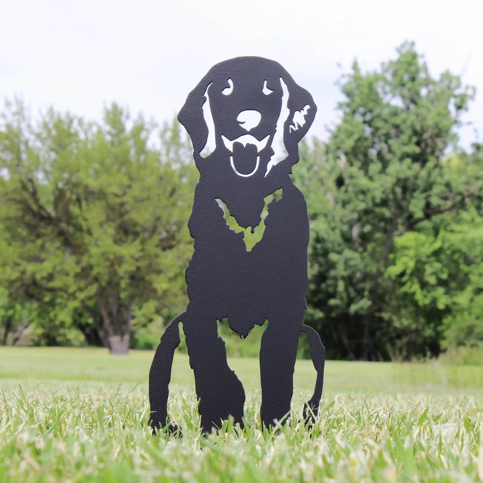 Handcrafted black metal silhouette of a Flat-Coated Retriever, standing in grass with greenery in the background.
