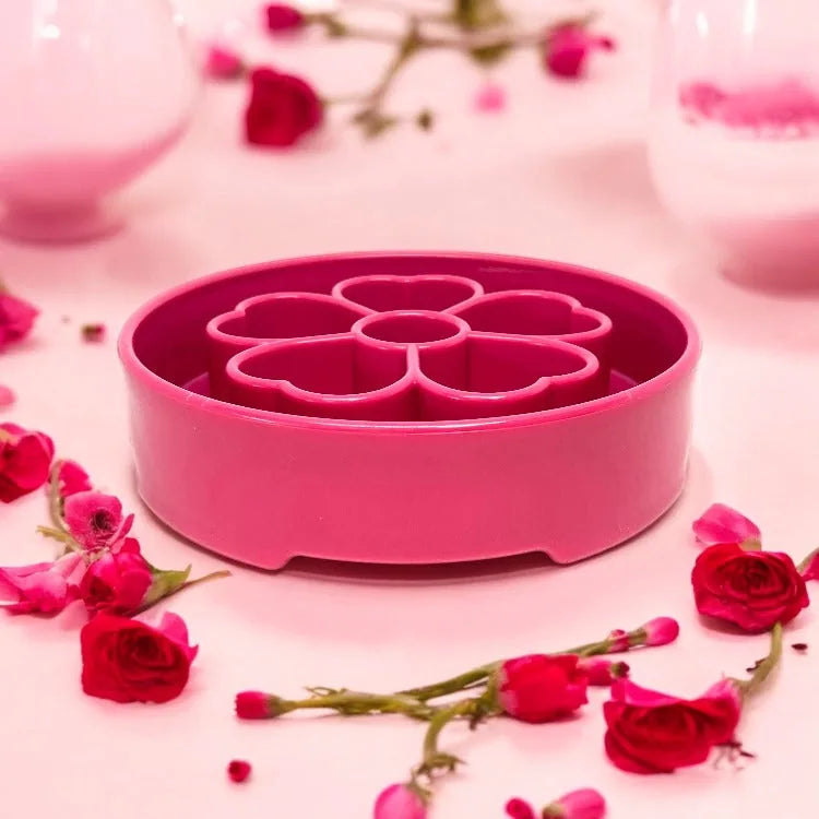 Pink flower-shaped slow feeder dog bowl with segmented chambers, surrounded by fresh flowers. Ideal for healthier eating.