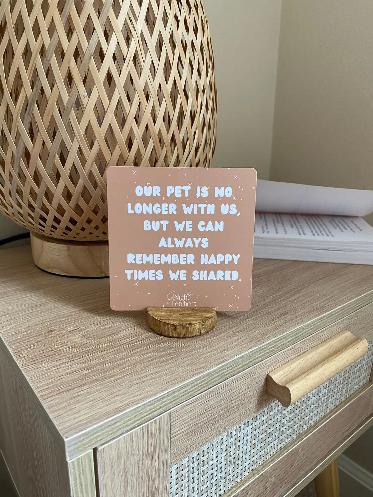 Peach affirmation card on a wooden stand, featuring a comforting message about pet loss, beside a woven lamp.