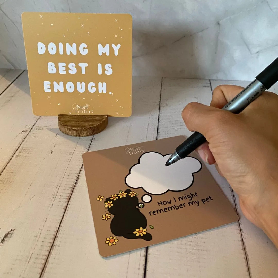 Brown comfort card with a black silhouette of a pet and a writing space, alongside a yellow affirmation card on a wooden s...