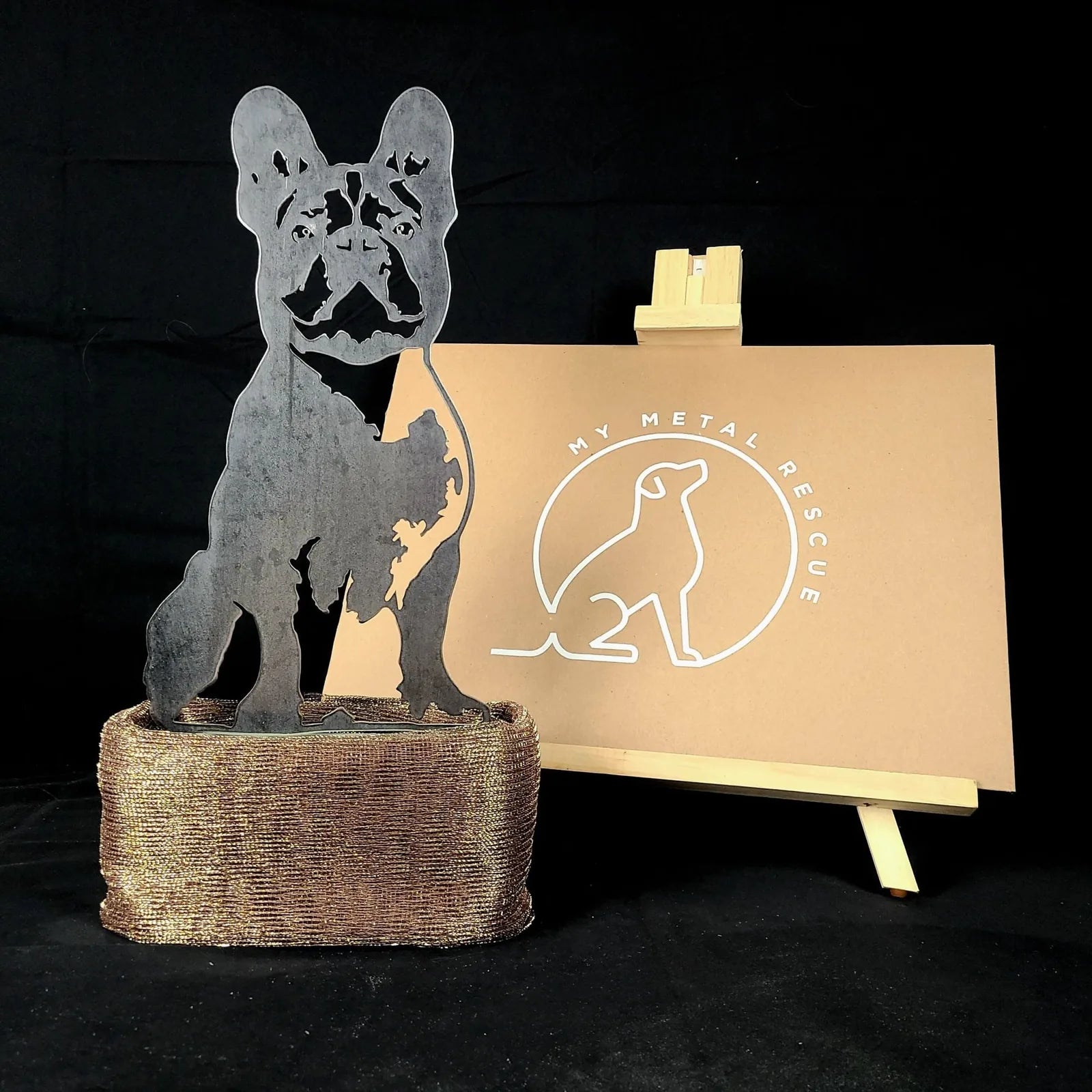 Handmade black metal silhouette of a French Bulldog atop a textured bronze base, showcased against a neutral backdrop.