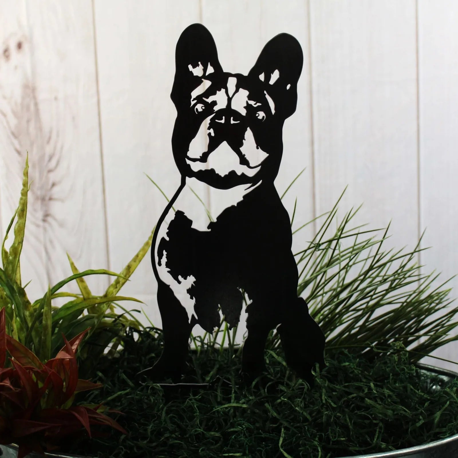 Handmade black metal art silhouette of a French Bulldog, showcasing detailed features among decorative greenery.