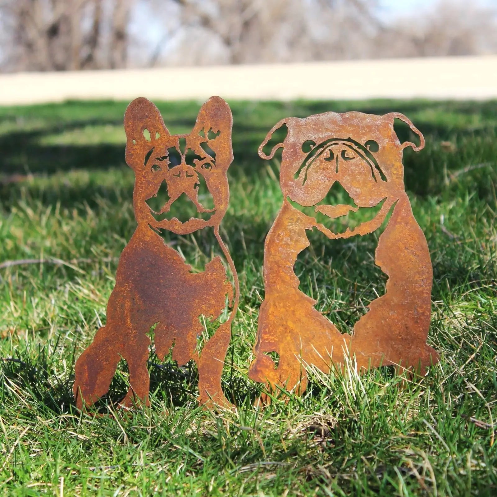 Rusty steel silhouettes of two French Bulldogs standing on green grass, showcasing handmade decorative art.