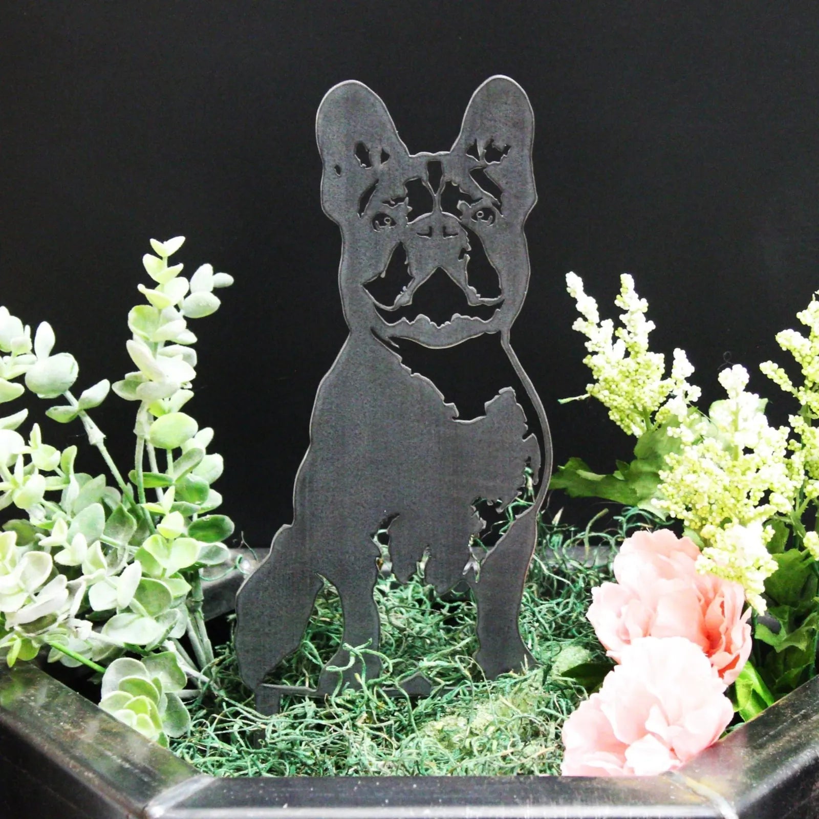 Handmade black metal art silhouette of a French Bulldog, surrounded by greenery and flowers in a decorative planter.