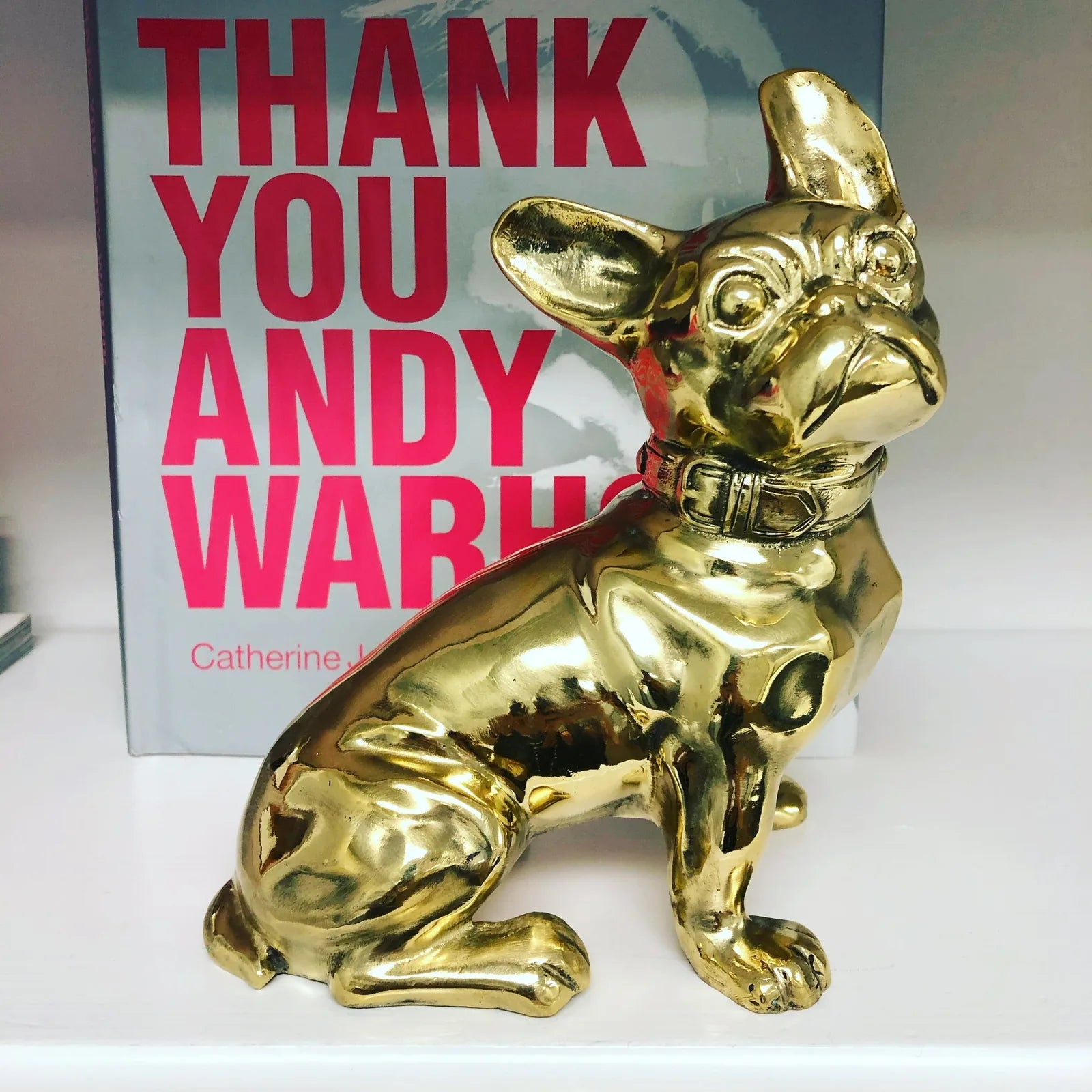 Brass French Bulldog sculpture with a glossy finish, sitting beside a brightly colored book.