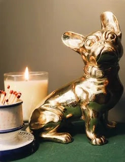 Handcrafted brass French Bulldog sculpture with a glossy finish beside a candle and a match holder.