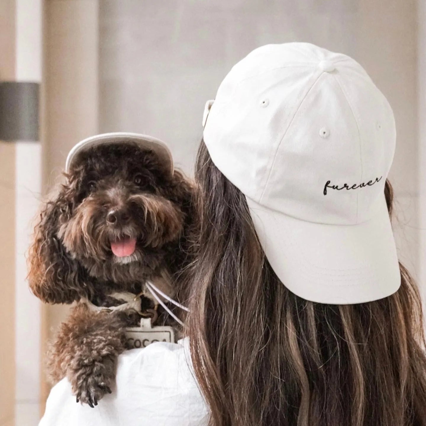 Matching white baseball hats with "furever" embroidery worn by a person and a happy dog, showcasing a stylish pet-parent l...