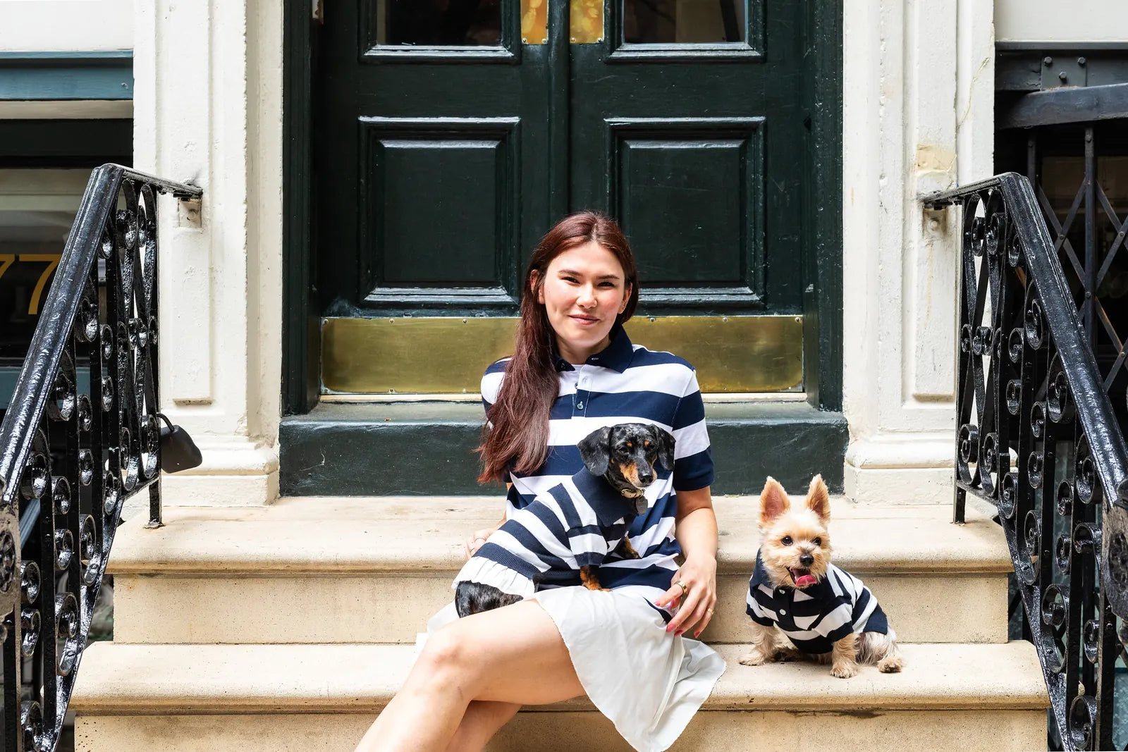 Stylish woman sitting on steps with two dogs, both in navy and white striped cashmere blend polos by BESPOKE PAWS.